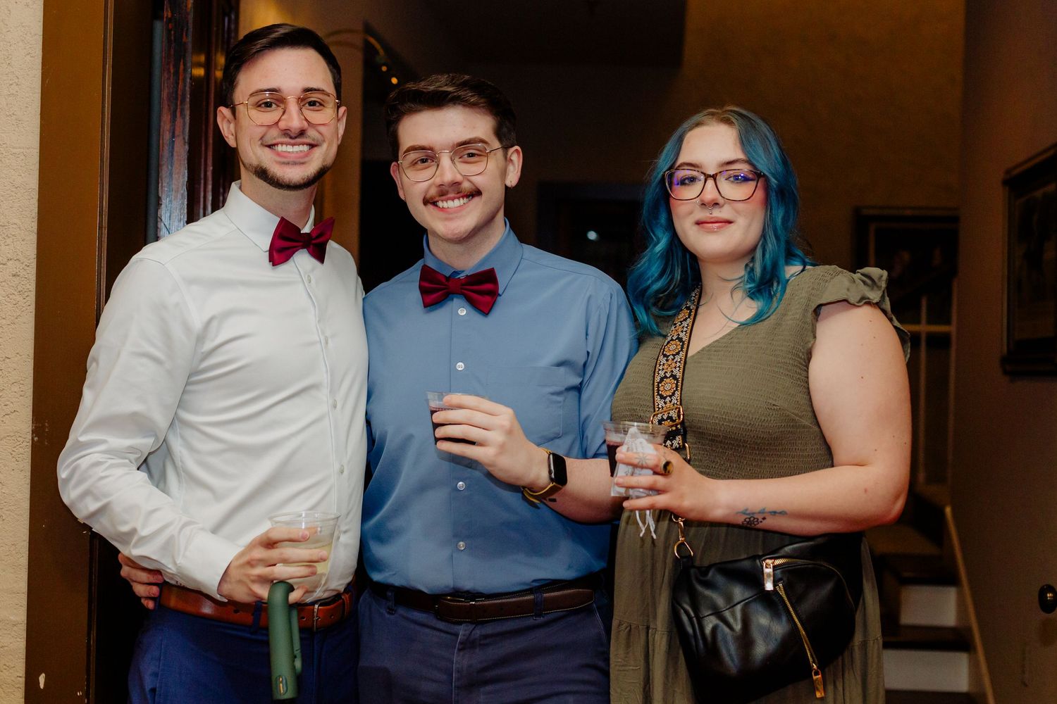 A group of formally dressed people stand together at an indoor event wearing bow ties and dressy attire.