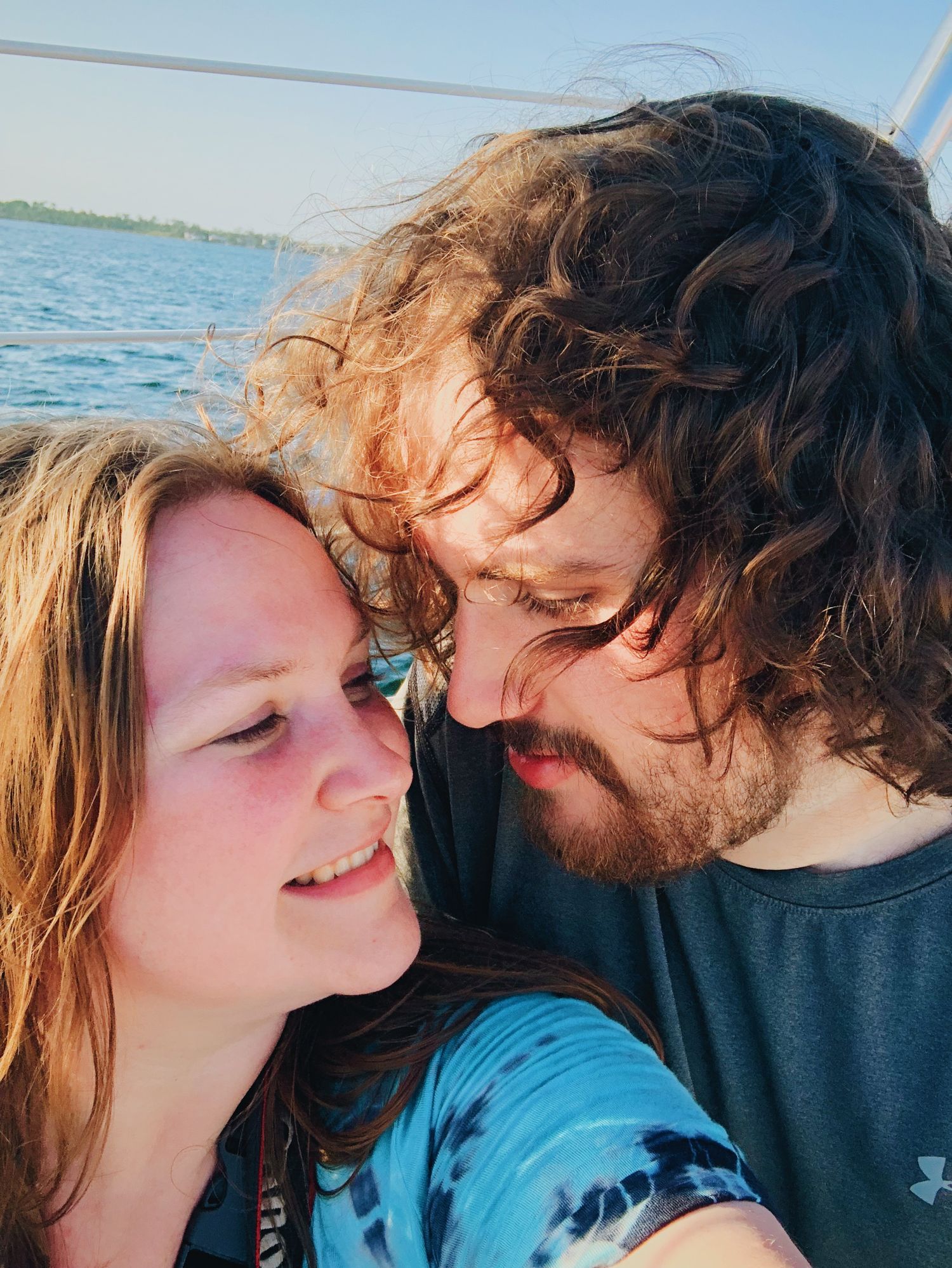 A romantic couple shares an intimate moment together against a bright blue ocean backdrop on a sunny day.