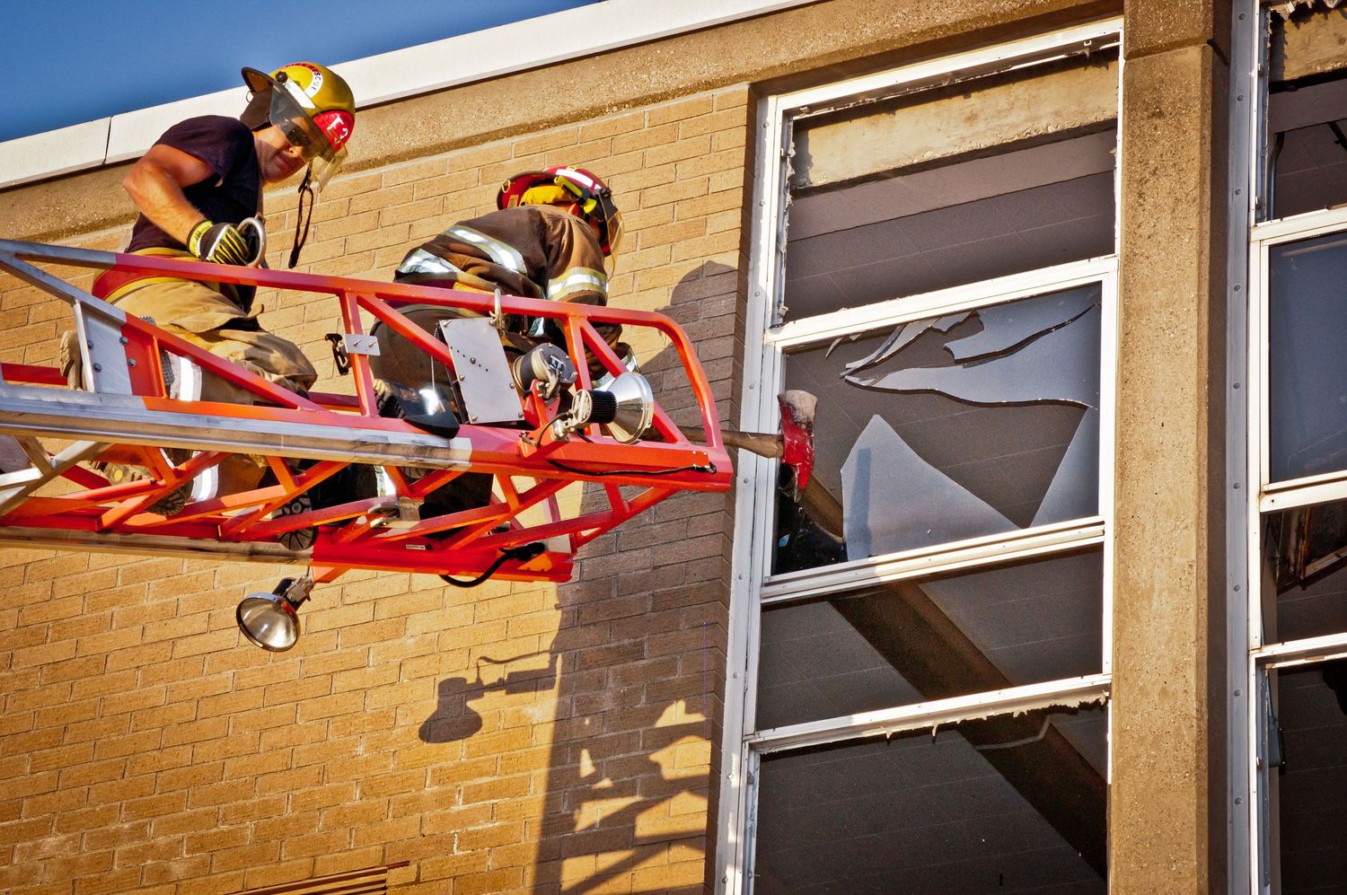 Firefighters on aerial ladder platform rescue operation at damaged building window during emergency response.