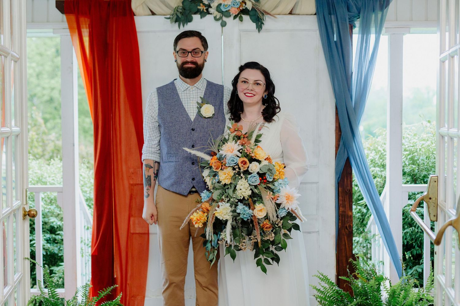 Wedding party poses in a bright conservatory with orange and blue curtains and floral arrangements.