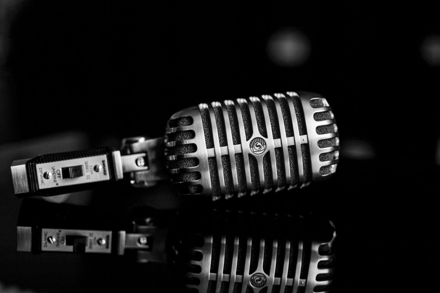 Vintage chrome retro microphone lying on a reflective black surface in dramatic black and white photography.