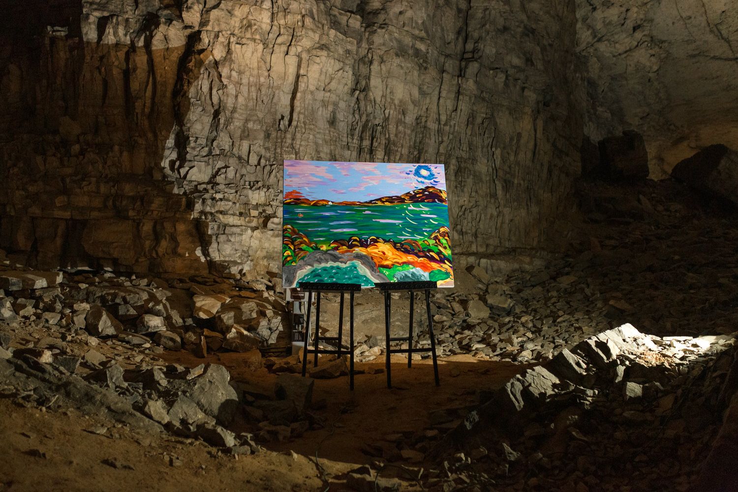 A vibrant painting on an easel displayed inside a dramatic cave with rocky walls and natural lighting.