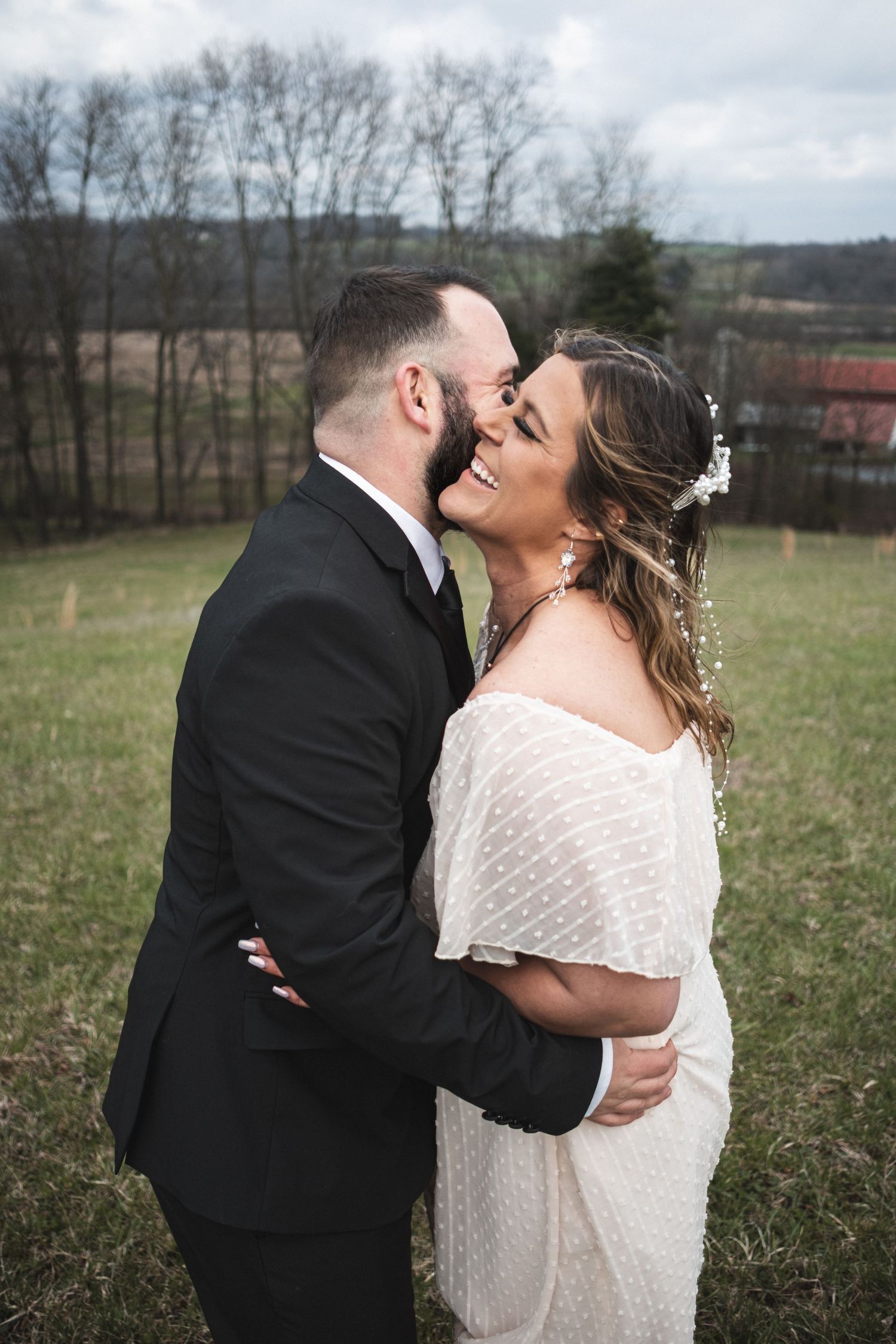 An engaged couple dances in a field, he in a suit, she in a white dress, sharing a joyful moment captured by McClure’s Photography.
