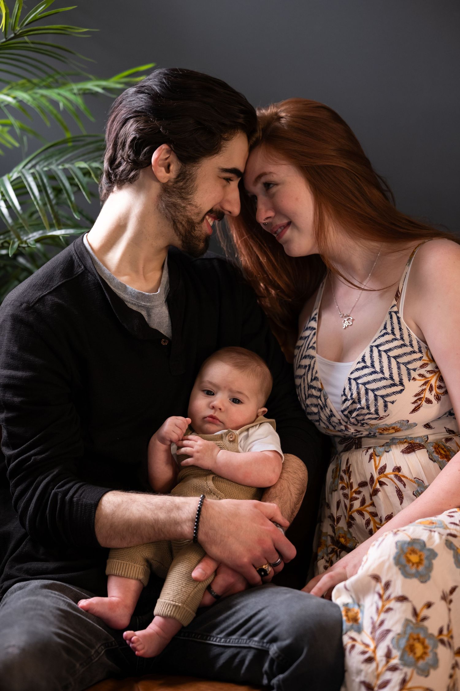A couple tenderly holds their baby, surrounded by greenery, in a heartfelt portrait by McClure’s Photography, exuding love and warmth.