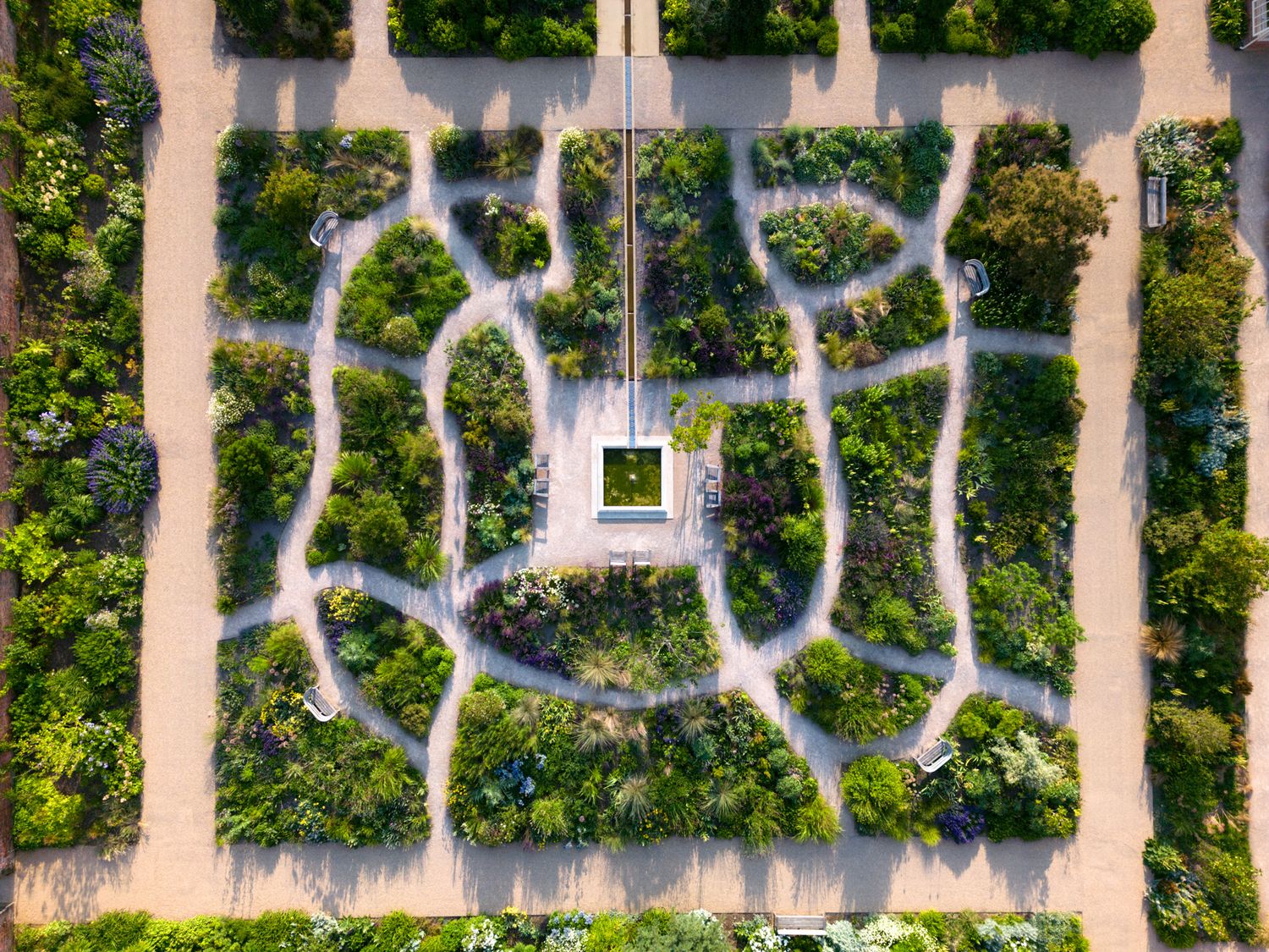 Aerial view of a symmetrical garden maze with winding paths and a central fountain surrounded by lush greenery.