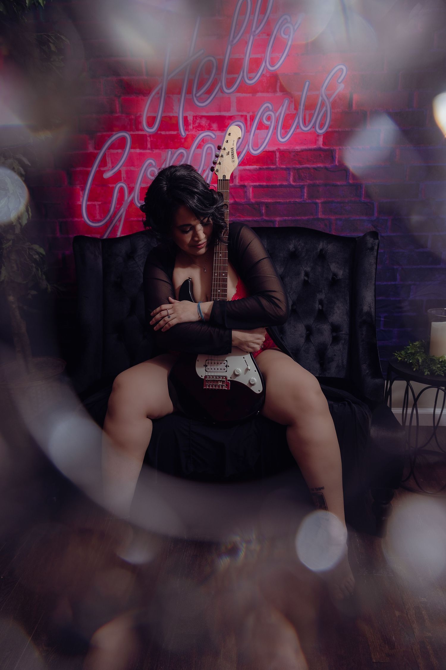 Dramatic portrait with electric guitar and neon sign against dark velvet couch.