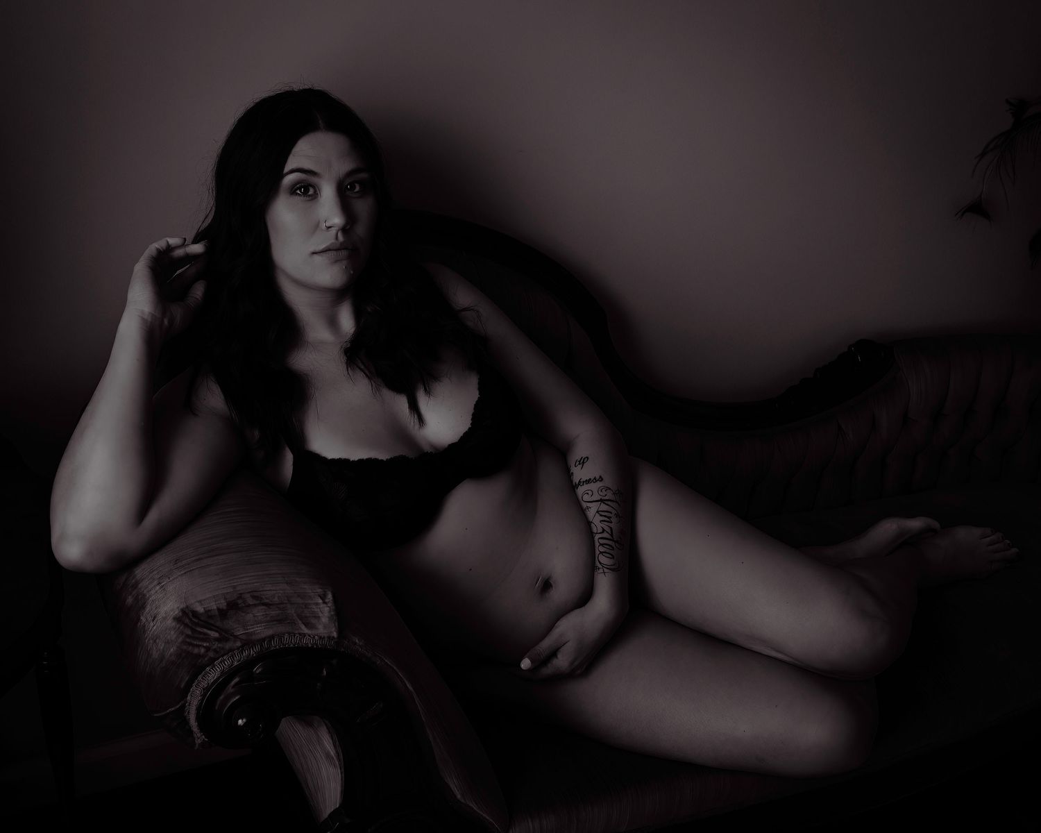 Moody boudoir portrait in dark tones featuring black lingerie on vintage furniture.
