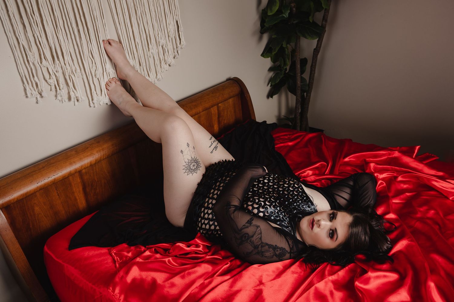 Boudoir photo on red satin sheets with black lace lingerie and macrame wall hanging.