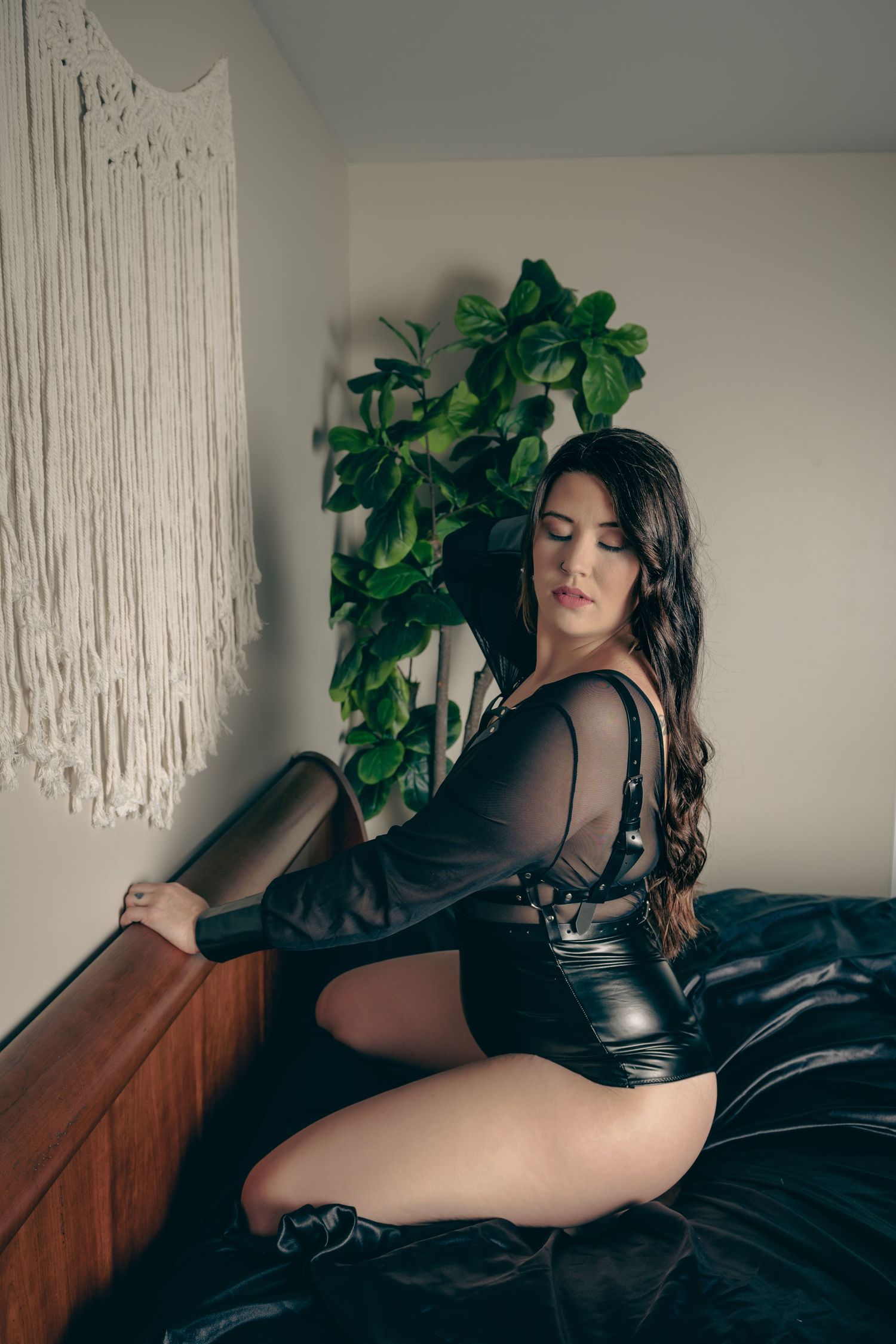 Artistic boudoir photo with black bodysuit against macrame and indoor plant decor.