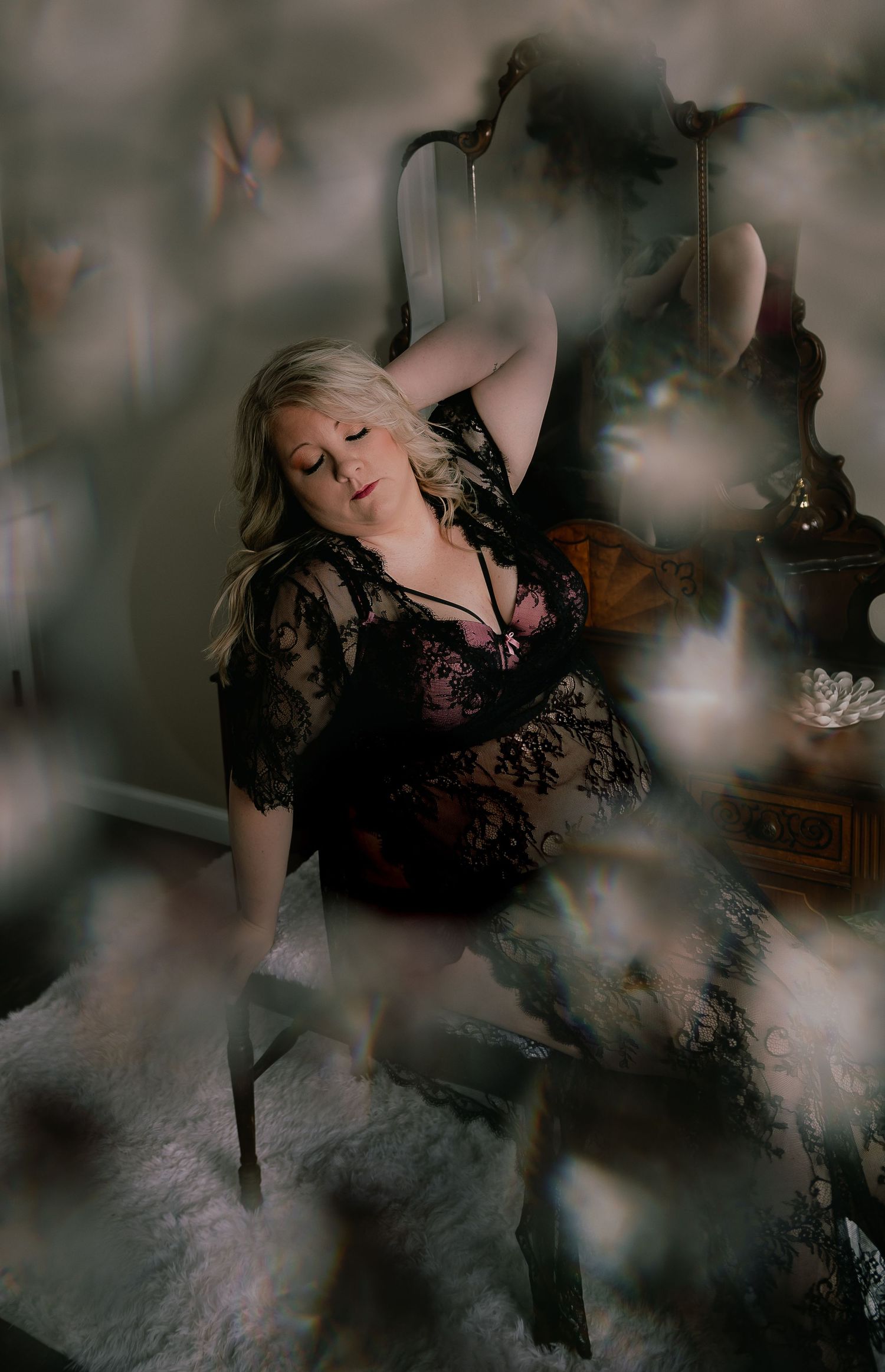 Artistic boudoir photograph with soft focus and dreamy overlays showing figure in black lace against antique furniture.