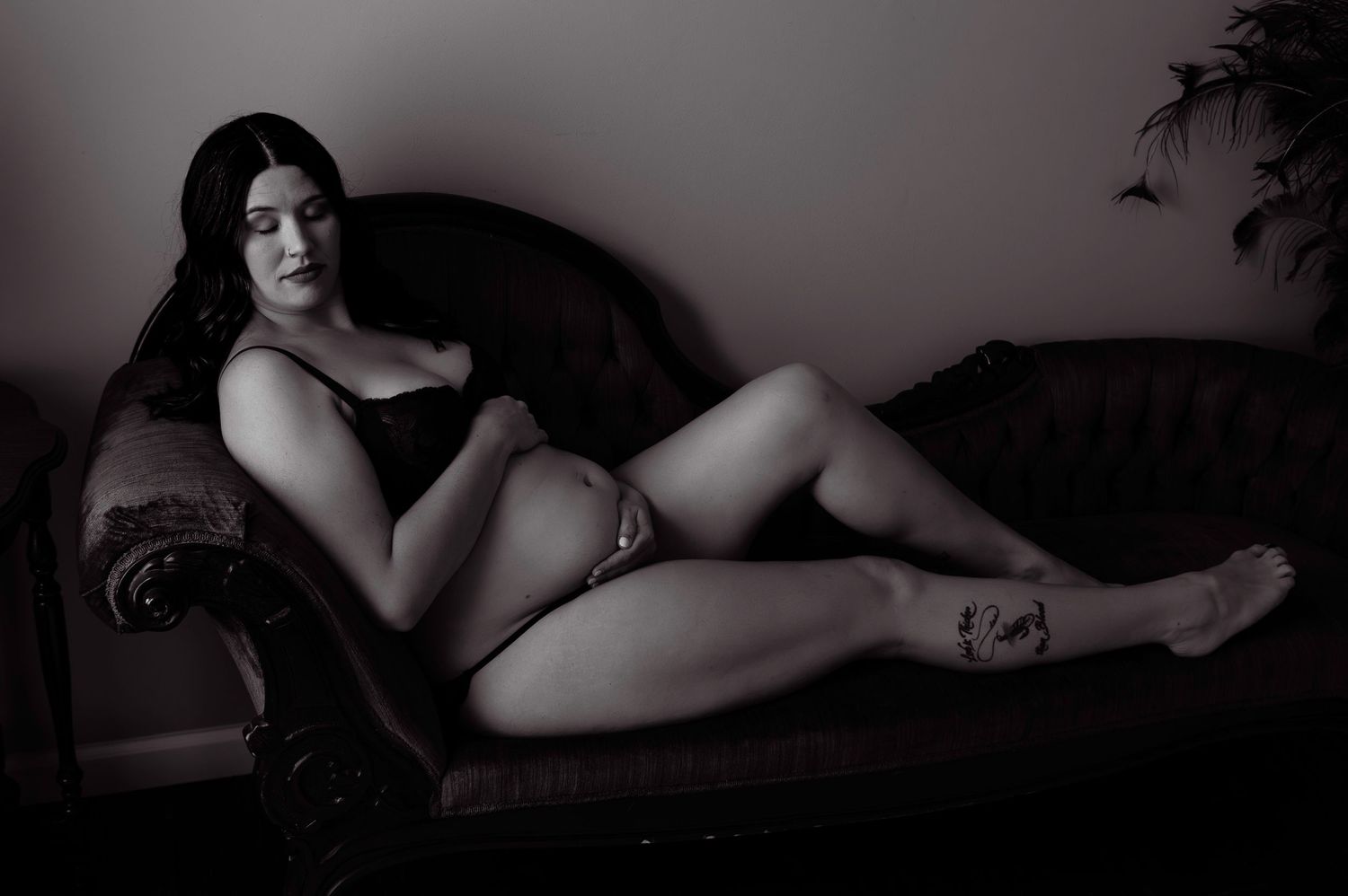 Vintage style boudoir portrait on dark leather sofa in dim lighting.