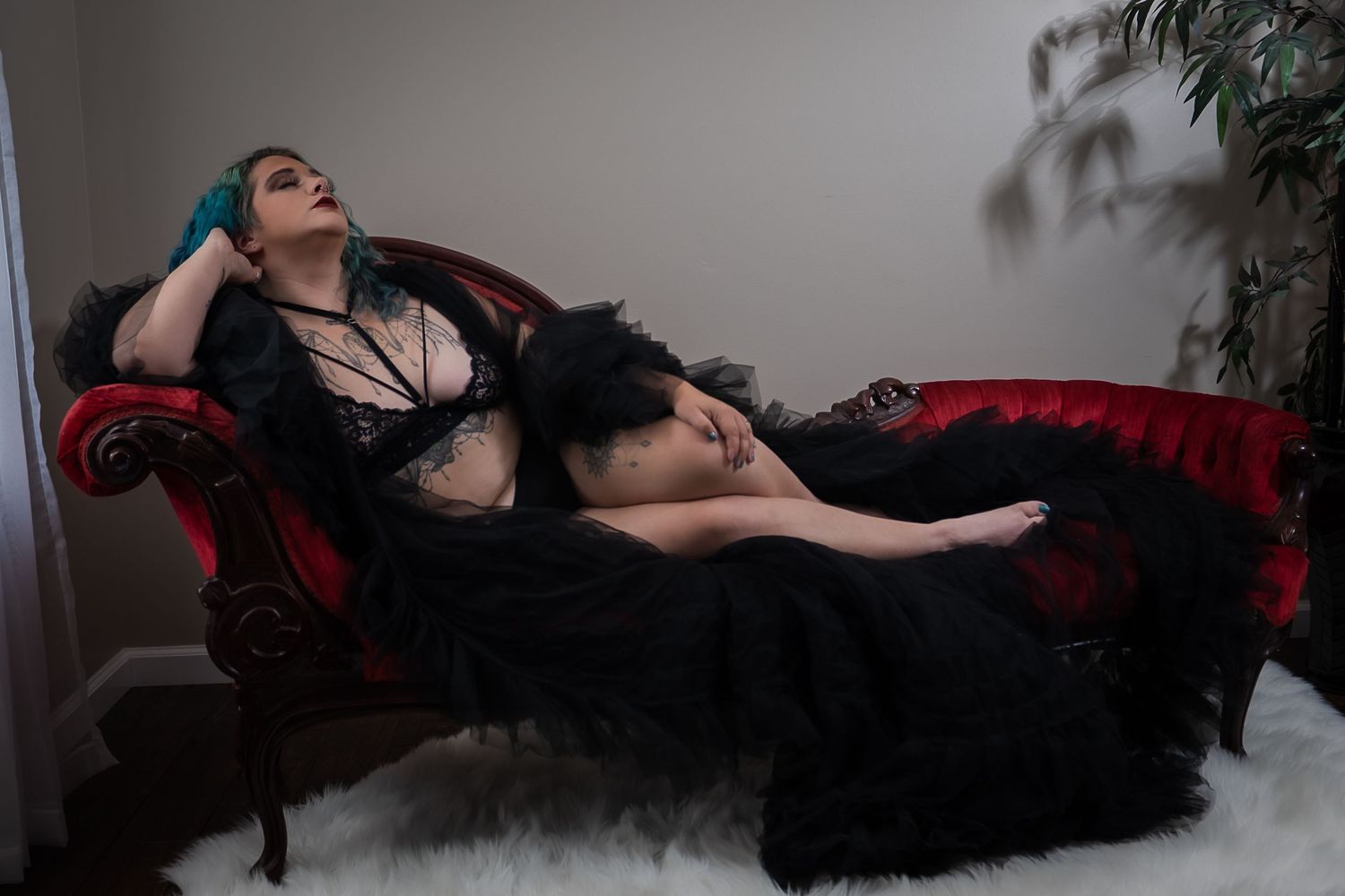 Dramatic boudoir portrait on red velvet chaise with black tulle gown.