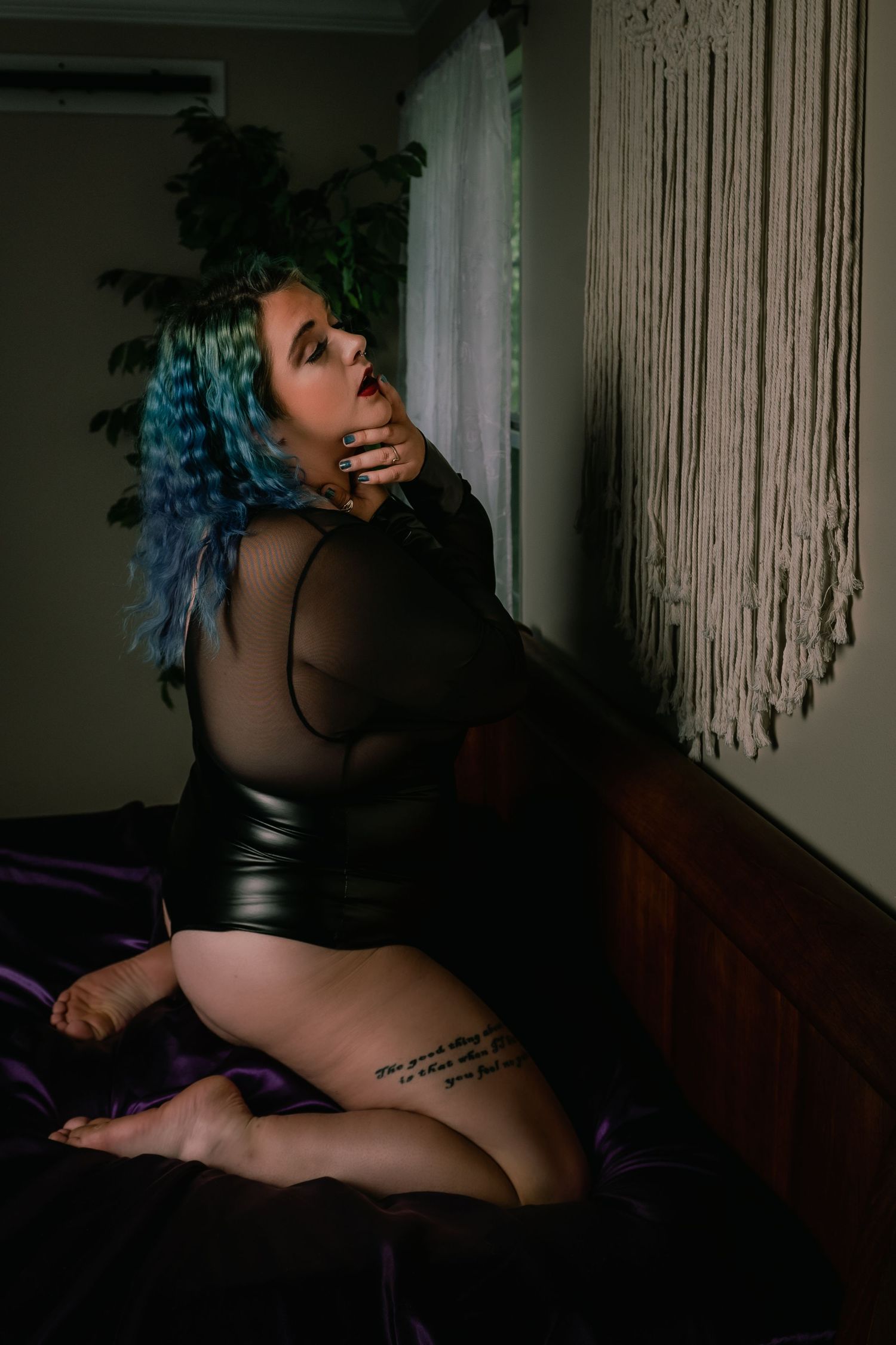 Alternative boudoir portrait featuring blue hair and mesh top against macrame backdrop.
