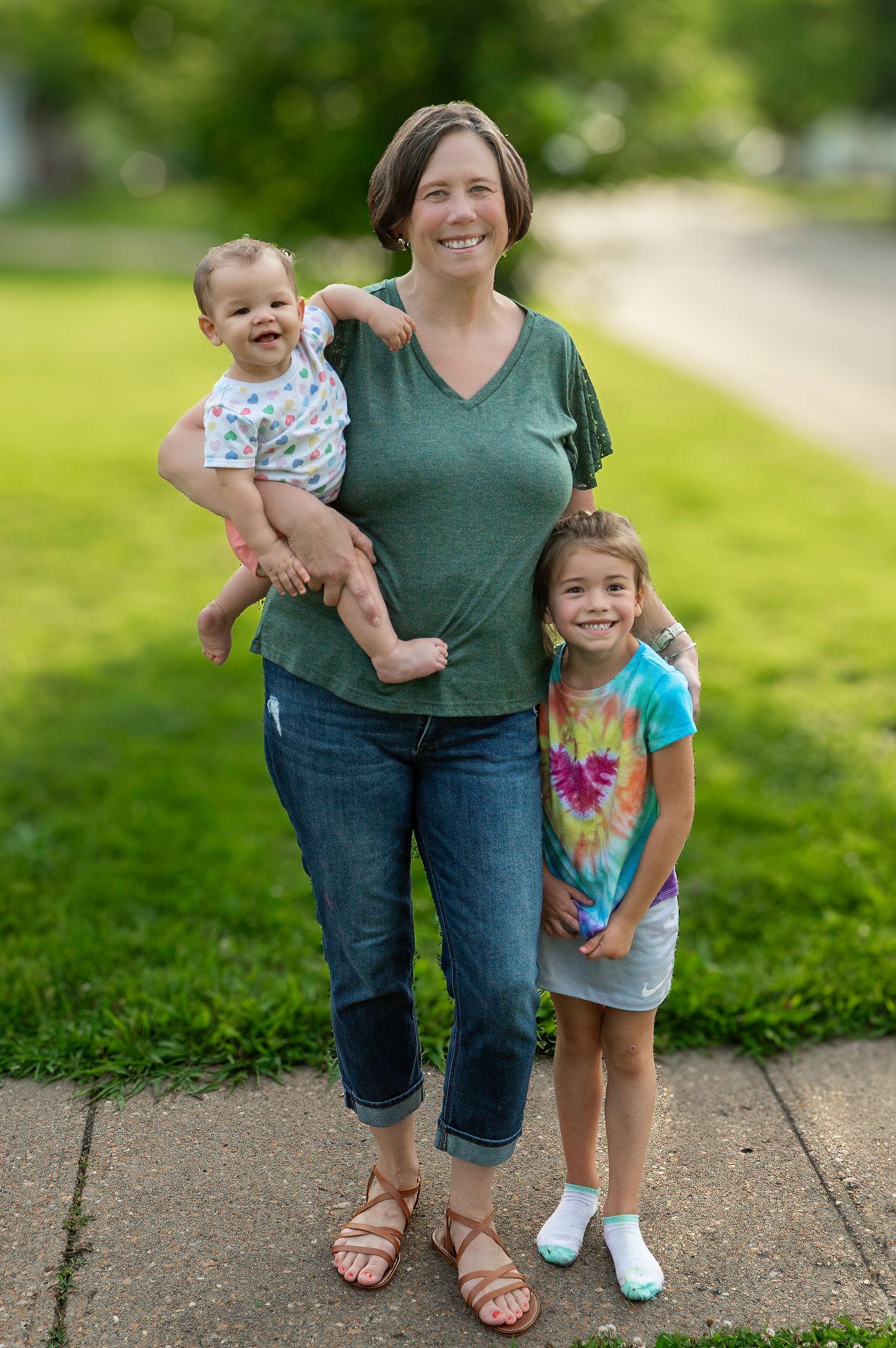 Family portrait outdoors on sidewalk with green grass background on sunny day.