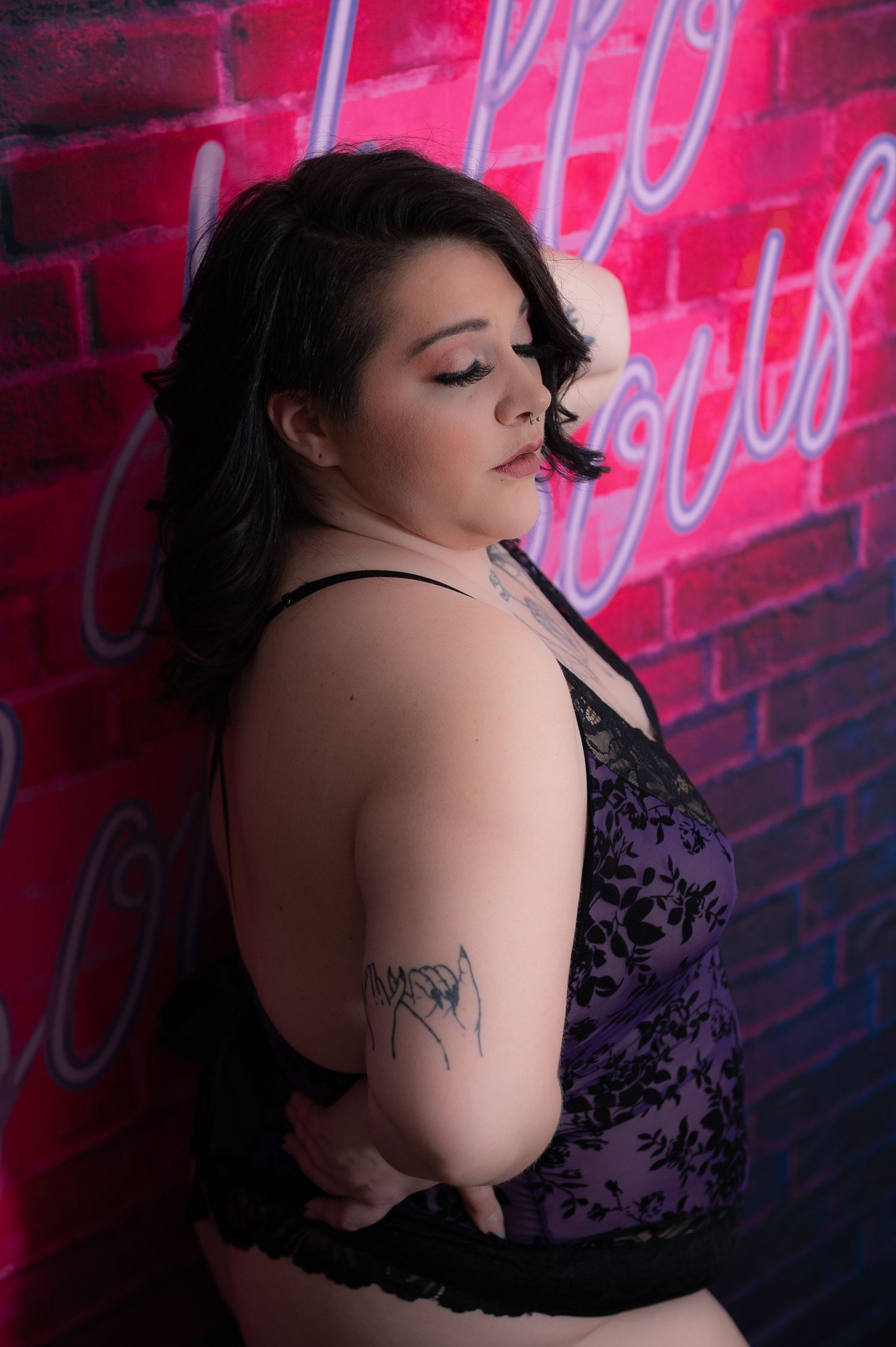 Moody portrait against brick wall with neon lighting in purple lace attire.
