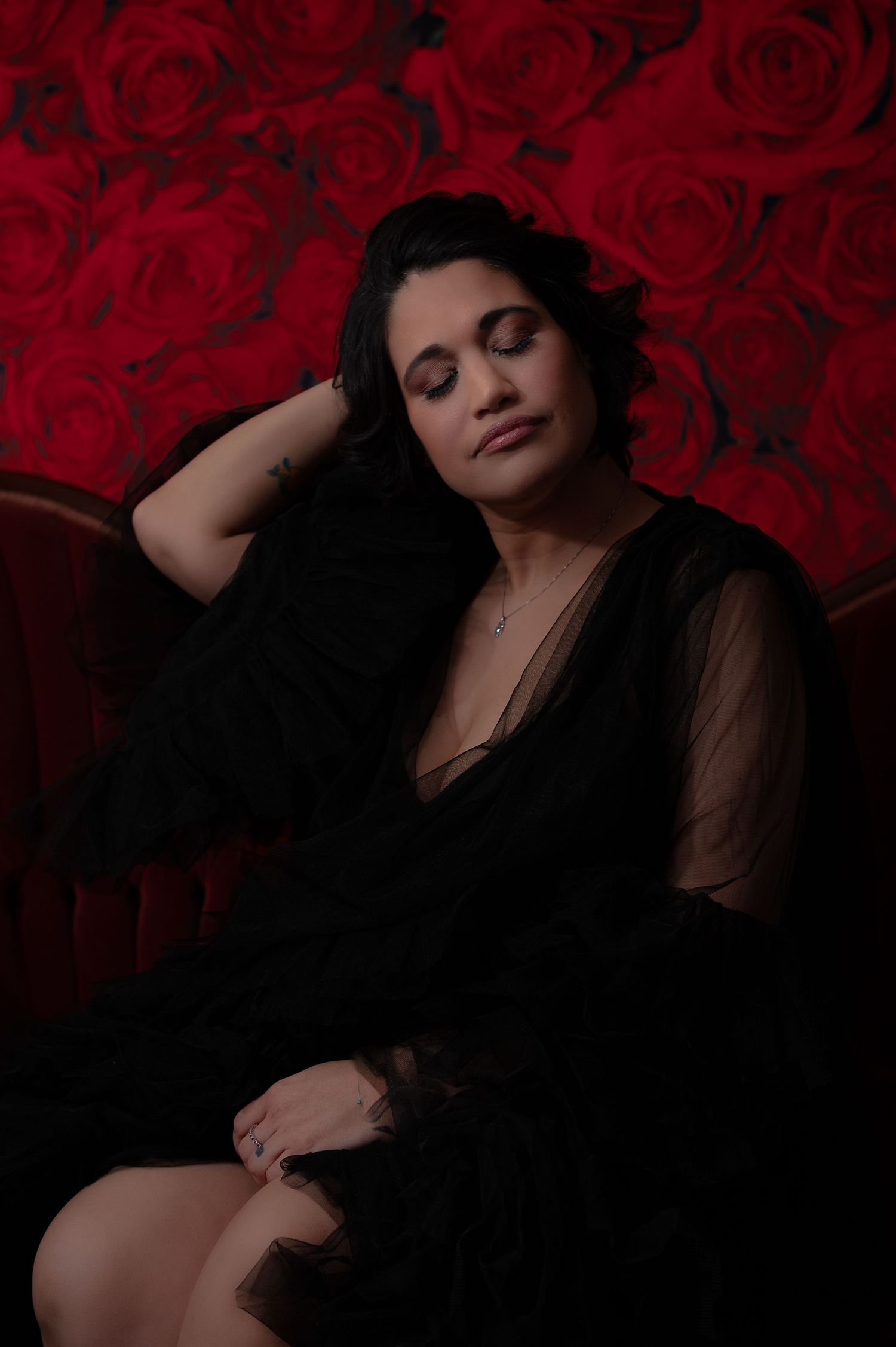 Elegant portrait against red rose backdrop with sheer black clothing.