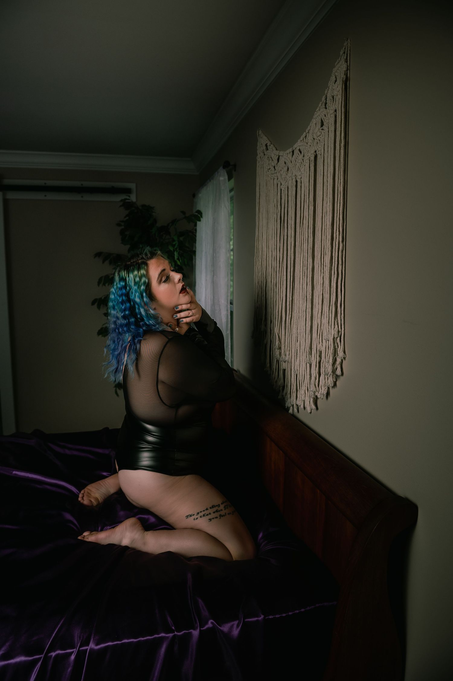 Artistic boudoir photo showing figure in black mesh against macrame wall hanging.