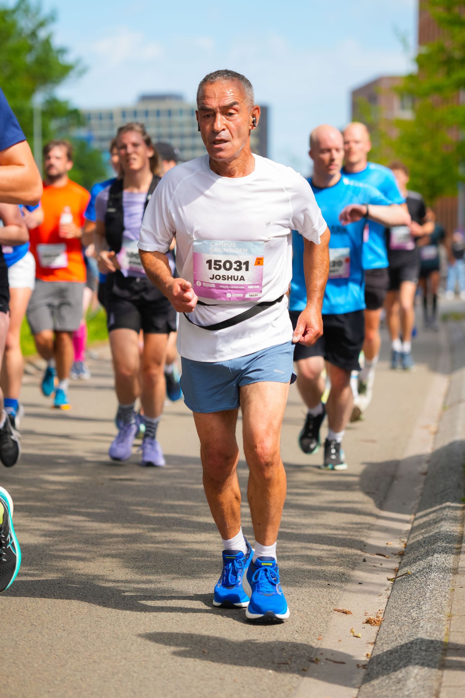 Runner #15031 Joshua competes in a city marathon wearing white shirt and blue shorts among other participants.