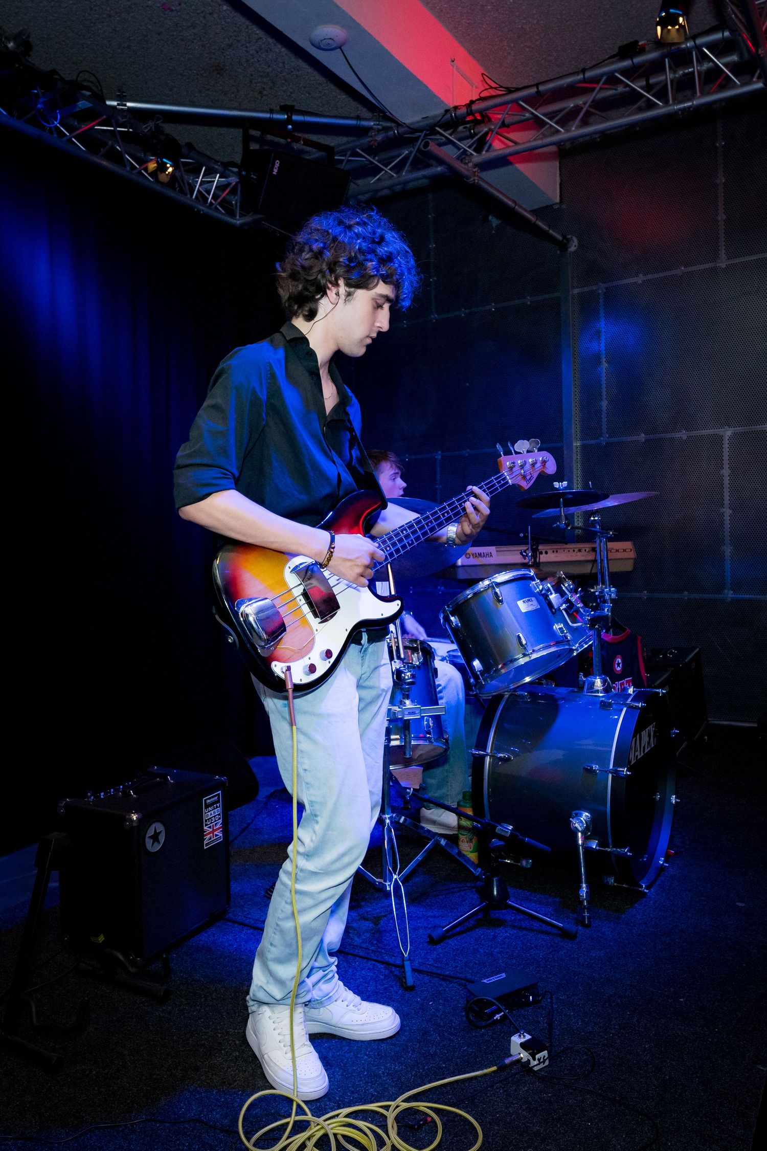 A musician performs on stage with a bass guitar under dramatic blue and red lighting during a live concert.