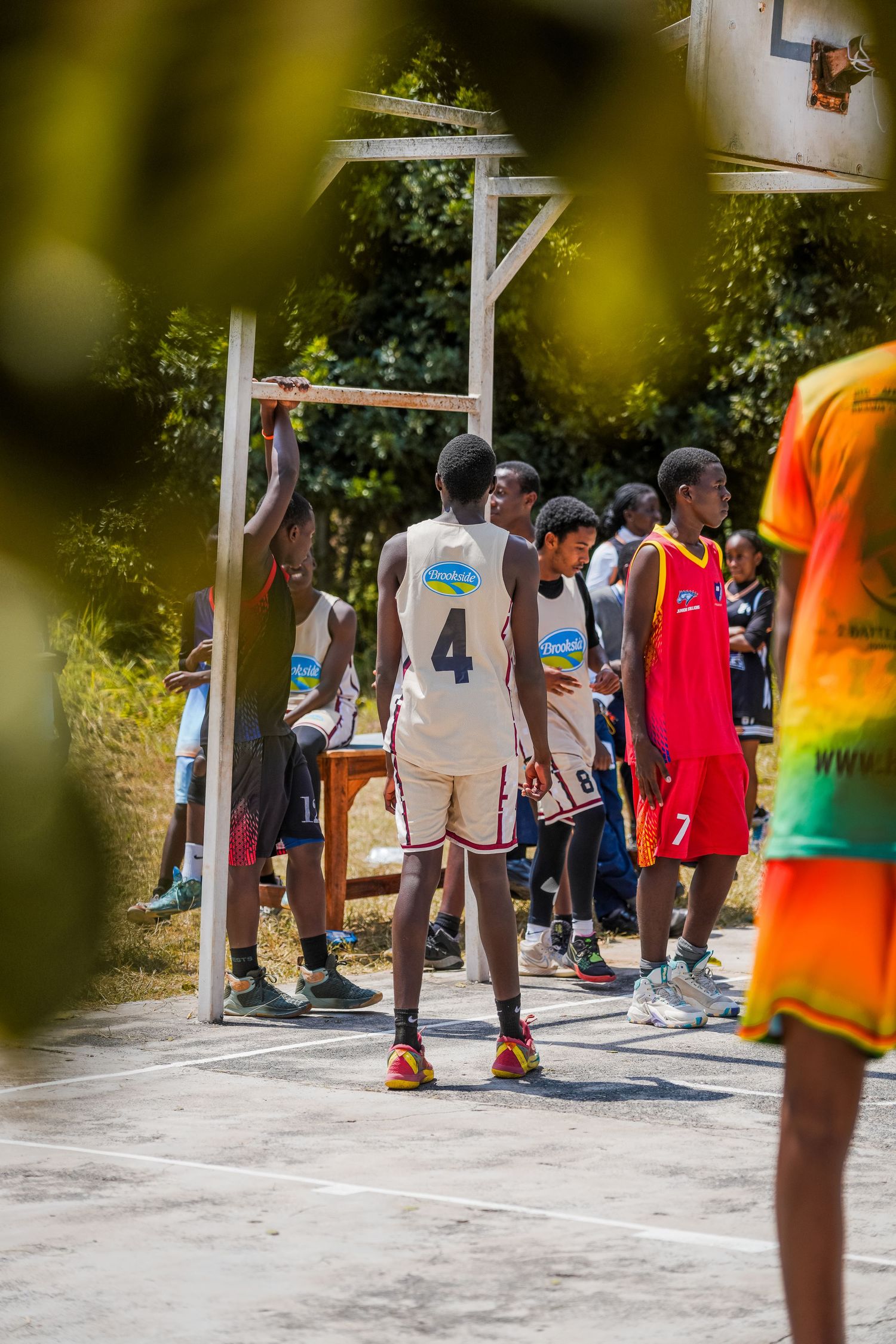 Young basketball players in jerseys compete on an outdoor court, with player number 4 standing near the hoop.