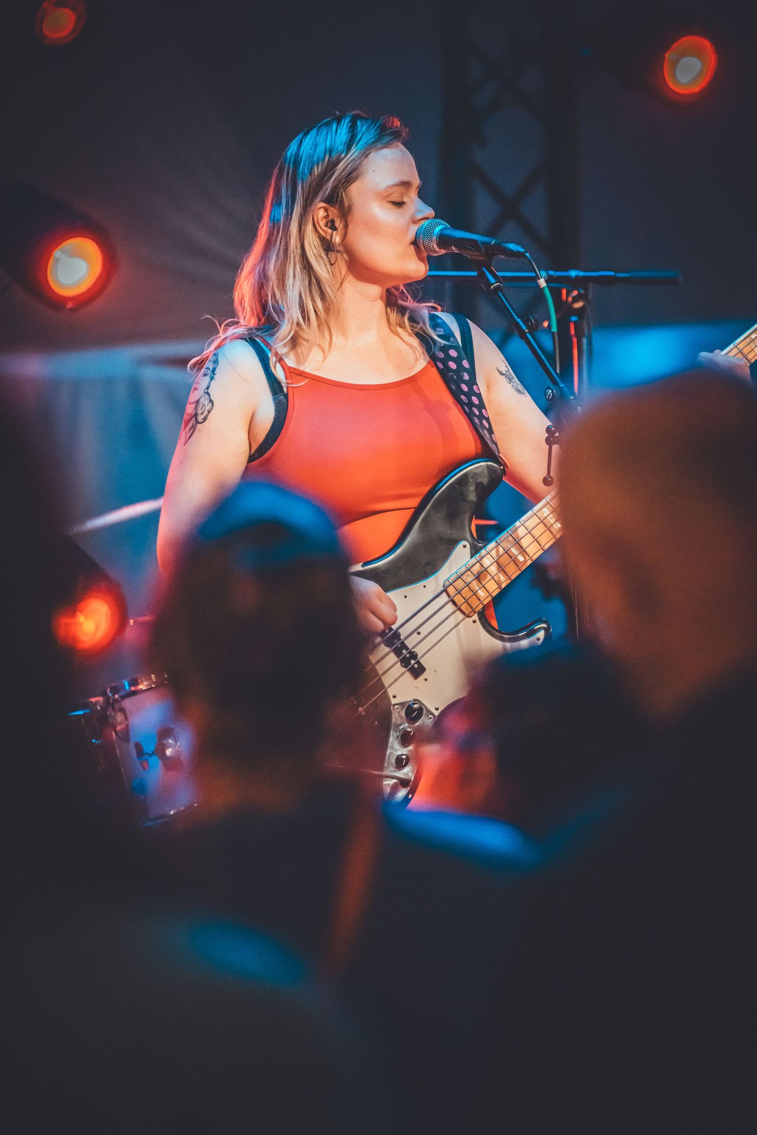 Musician performs energetically with bass guitar under dramatic red and blue concert lighting on stage.
