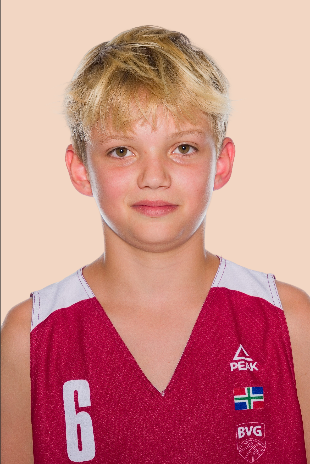 Young basketball player with short blond hair wearing a red number 6 BVG jersey with Peak logo, posing against a peach background.
