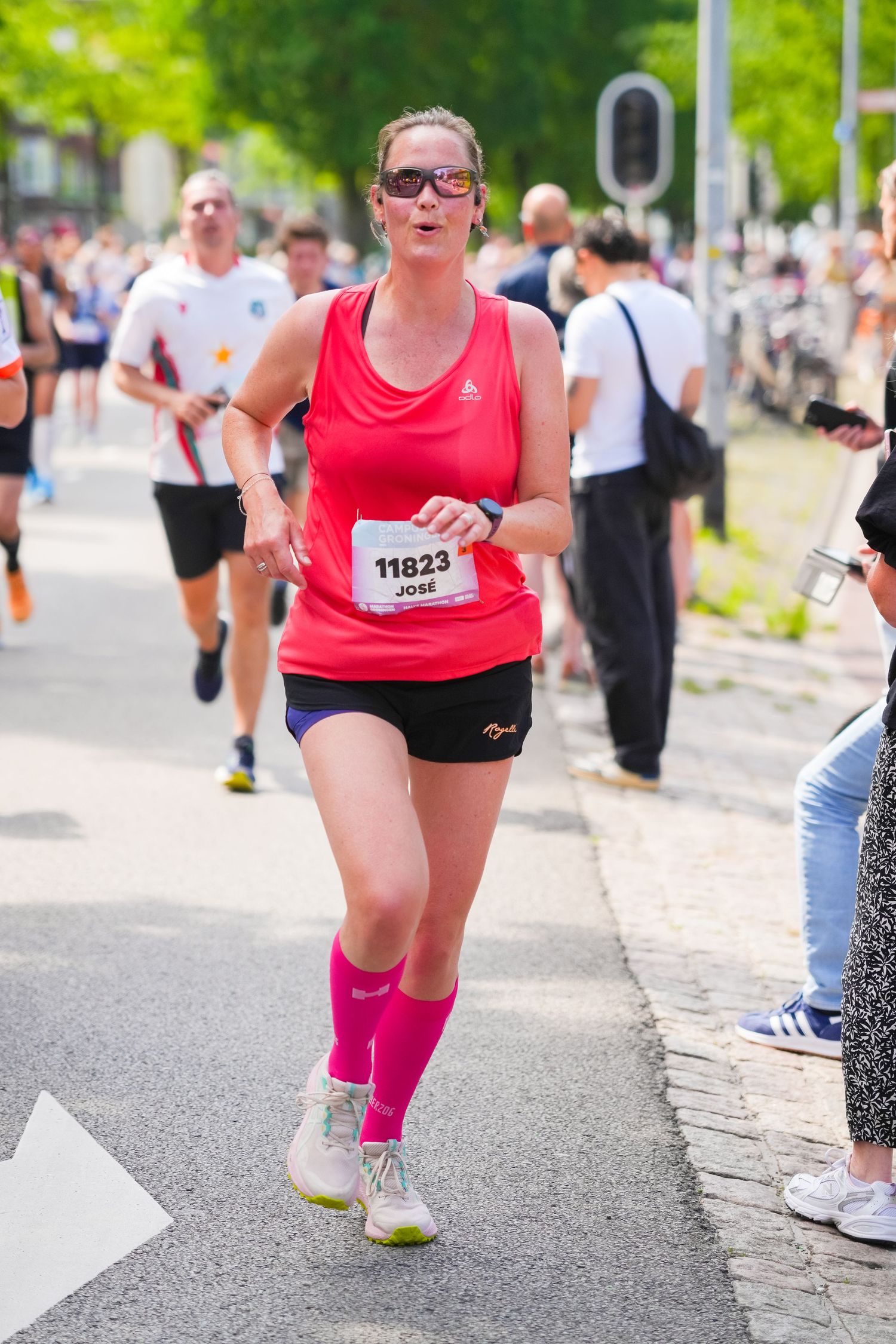 Woman wearing bib number 11823 running in a marathon, dressed in pink tank top, shorts, and knee-high socks.