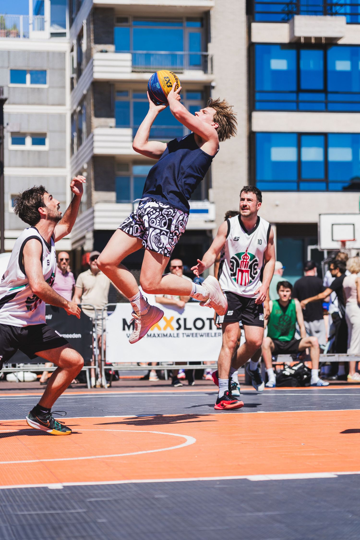 A male basketball player leaps to catch the ball during an outdoor 3x3 street basketball game on a sunny day.
