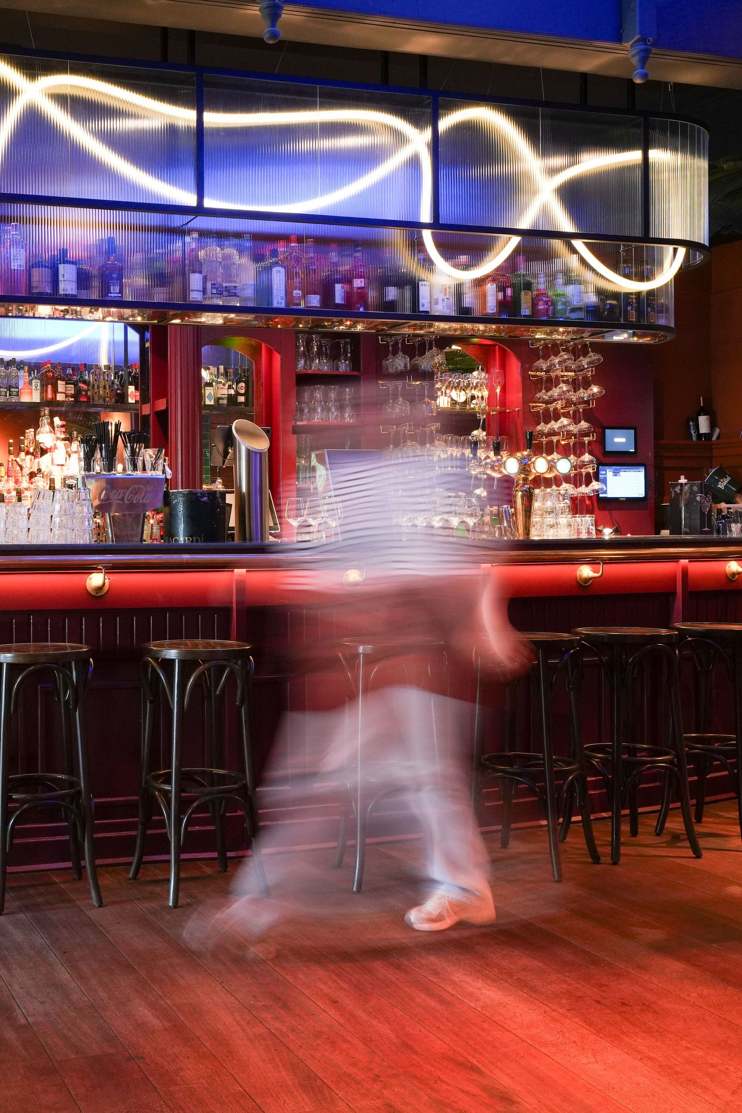 Blurred motion of bartender working at a vibrant red bar with neon lights and bar stools in a nightclub.