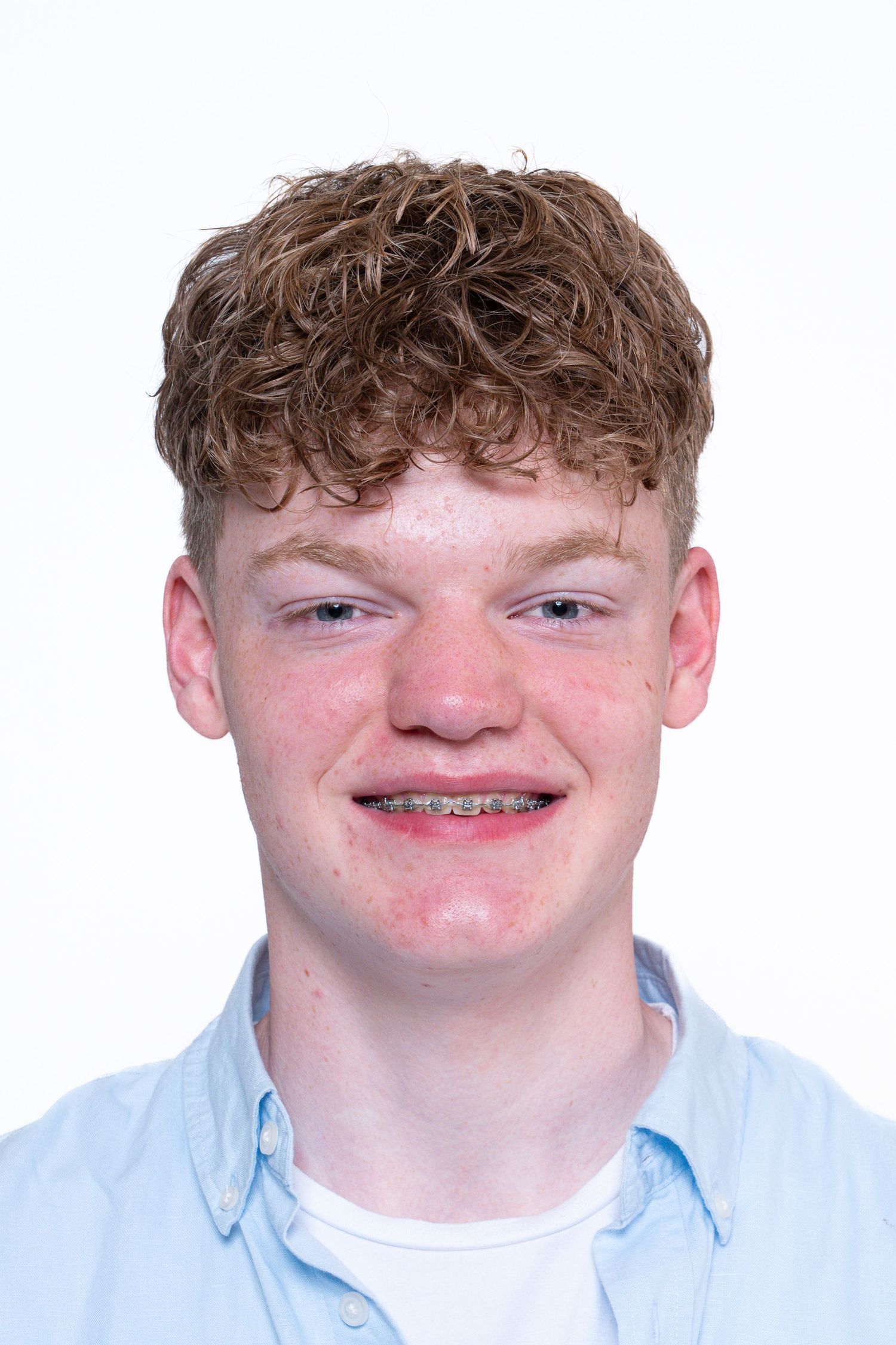Portrait of a person with curly brown hair wearing a light blue button-down shirt and braces, against a white background.