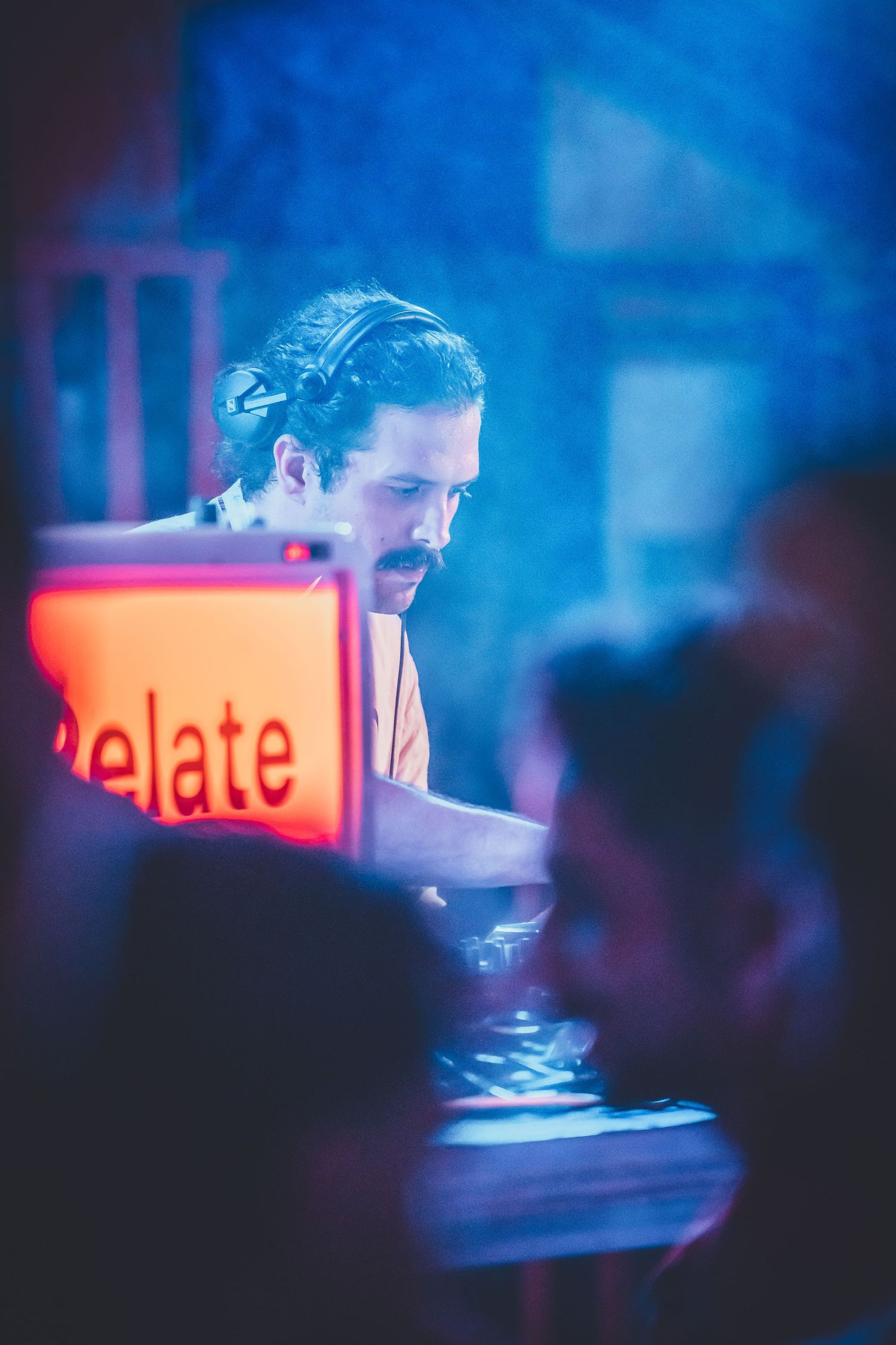 A DJ performs at a nightclub with glowing orange signage and blue atmospheric lighting in the background.