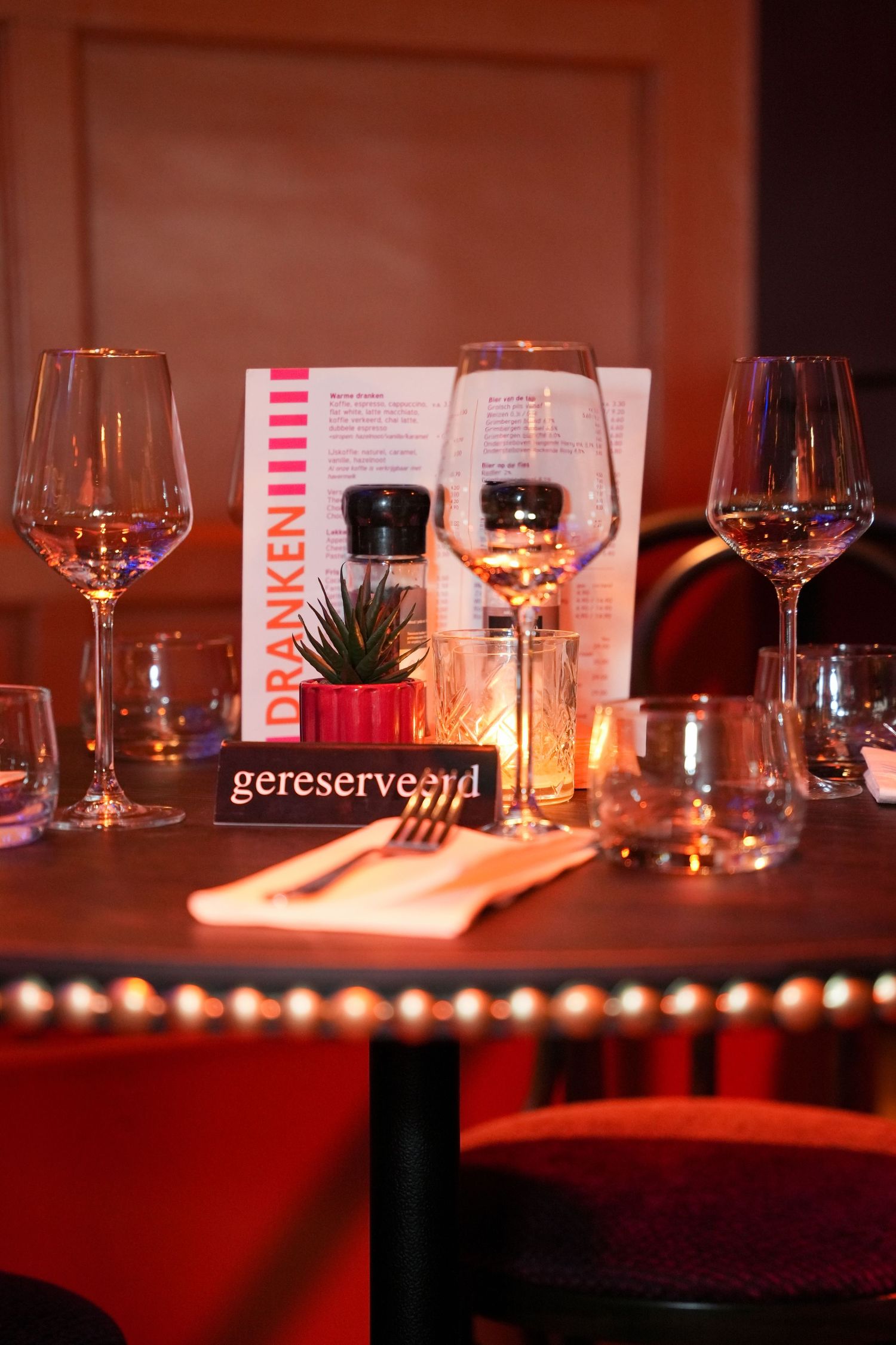 Elegant restaurant table set with wine glasses, candle, menu, and a reserved sign in warm red ambient lighting.