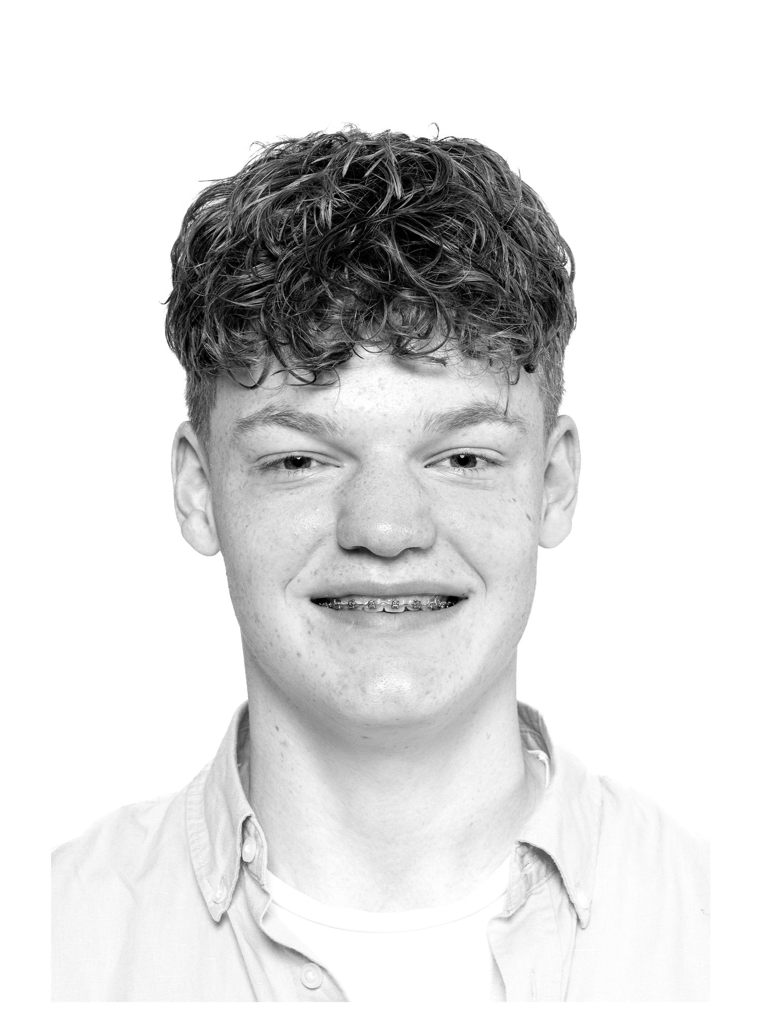 Black and white portrait headshot showing a young person with curly hair and braces wearing a white collared shirt.