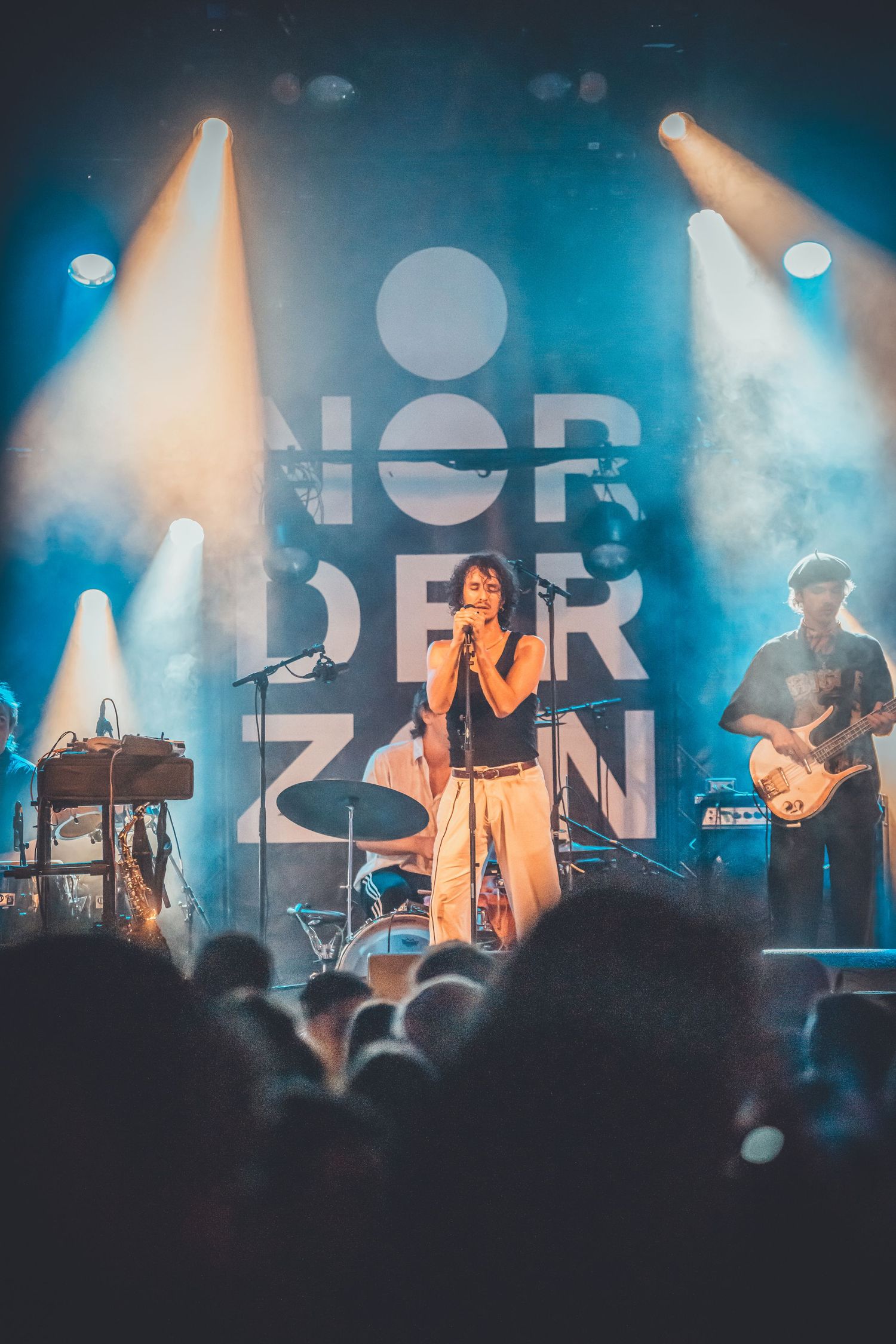 Live concert scene with stage lighting illuminating performers through atmospheric blue and white spotlights.