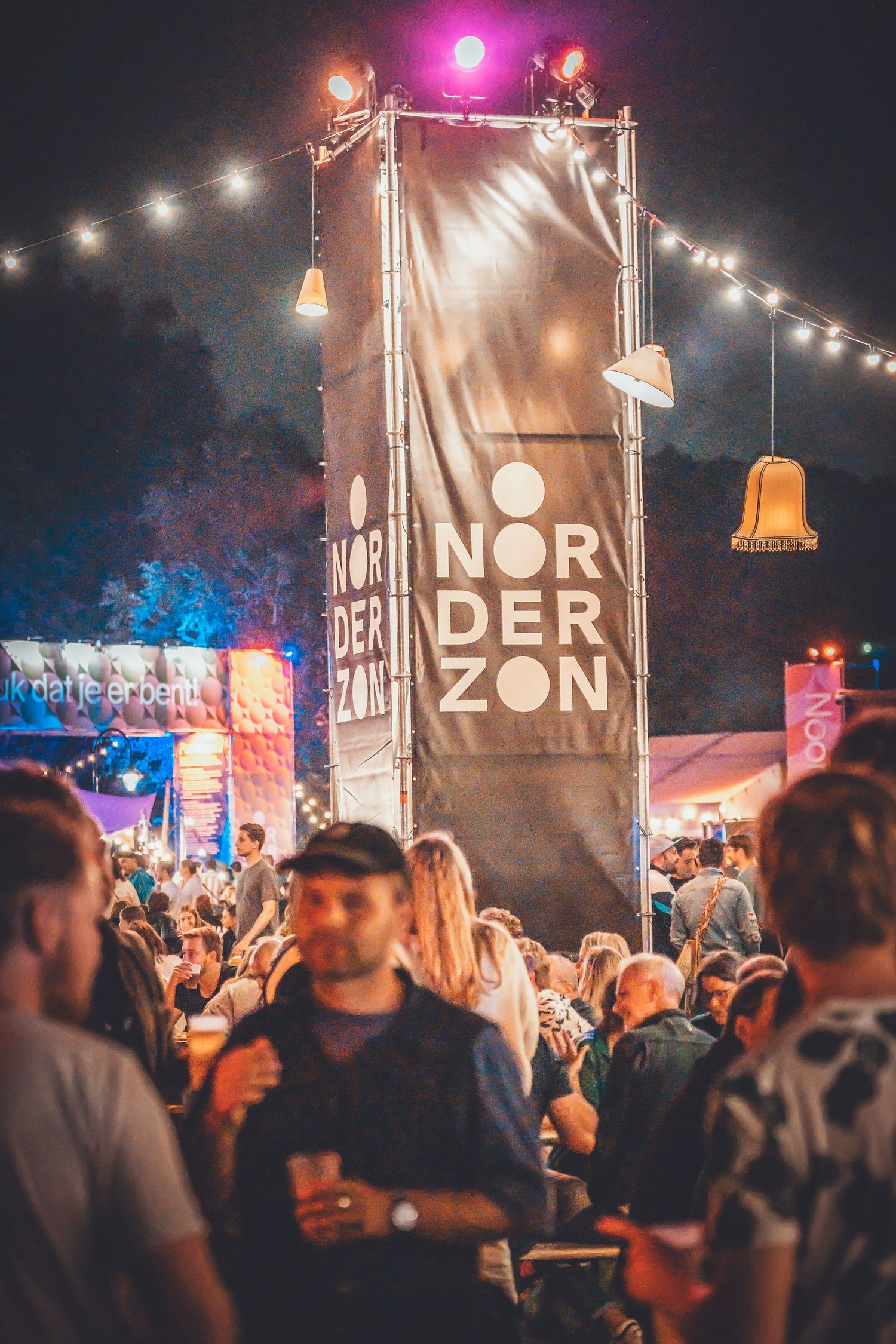 Crowded nighttime festival scene with illuminated Norderzon signage and hanging lantern decorations at outdoor event.