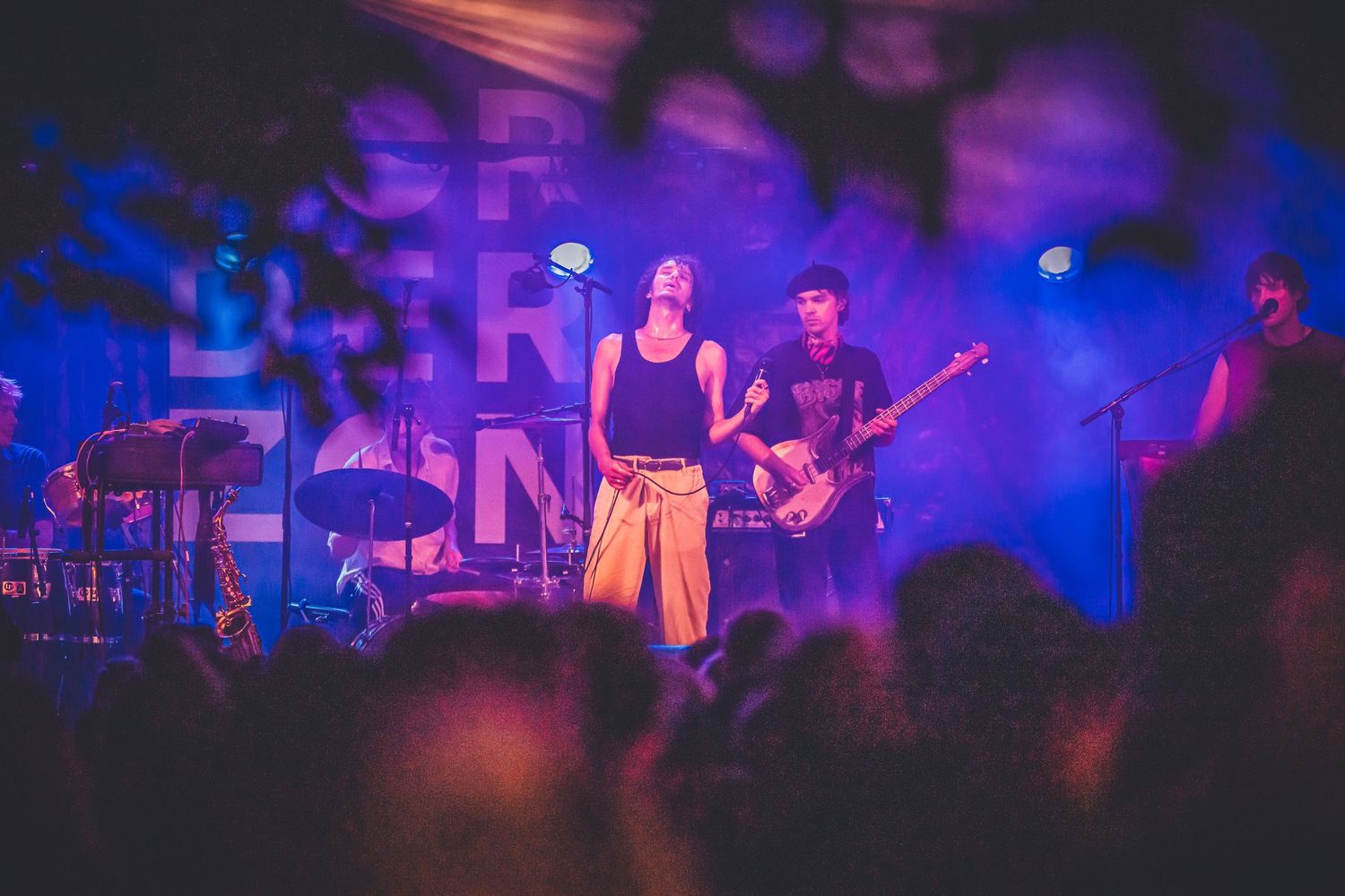 A band performs on stage bathed in vibrant purple and blue lighting during a live concert performance.