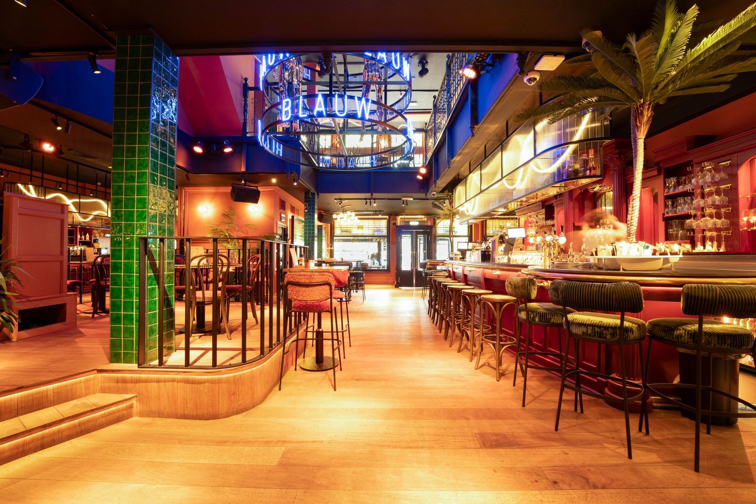 Stylish bar interior with green tile columns, bar stools, warm lighting, and tropical palm decor.