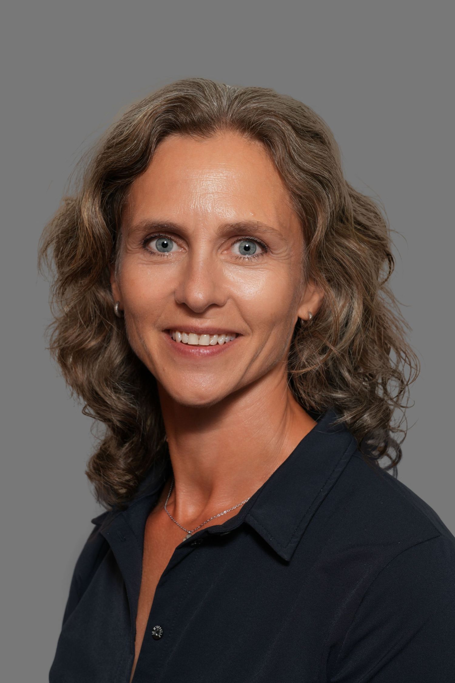 Professional headshot of a smiling woman with blue eyes and curly brown hair wearing a dark navy blouse.
