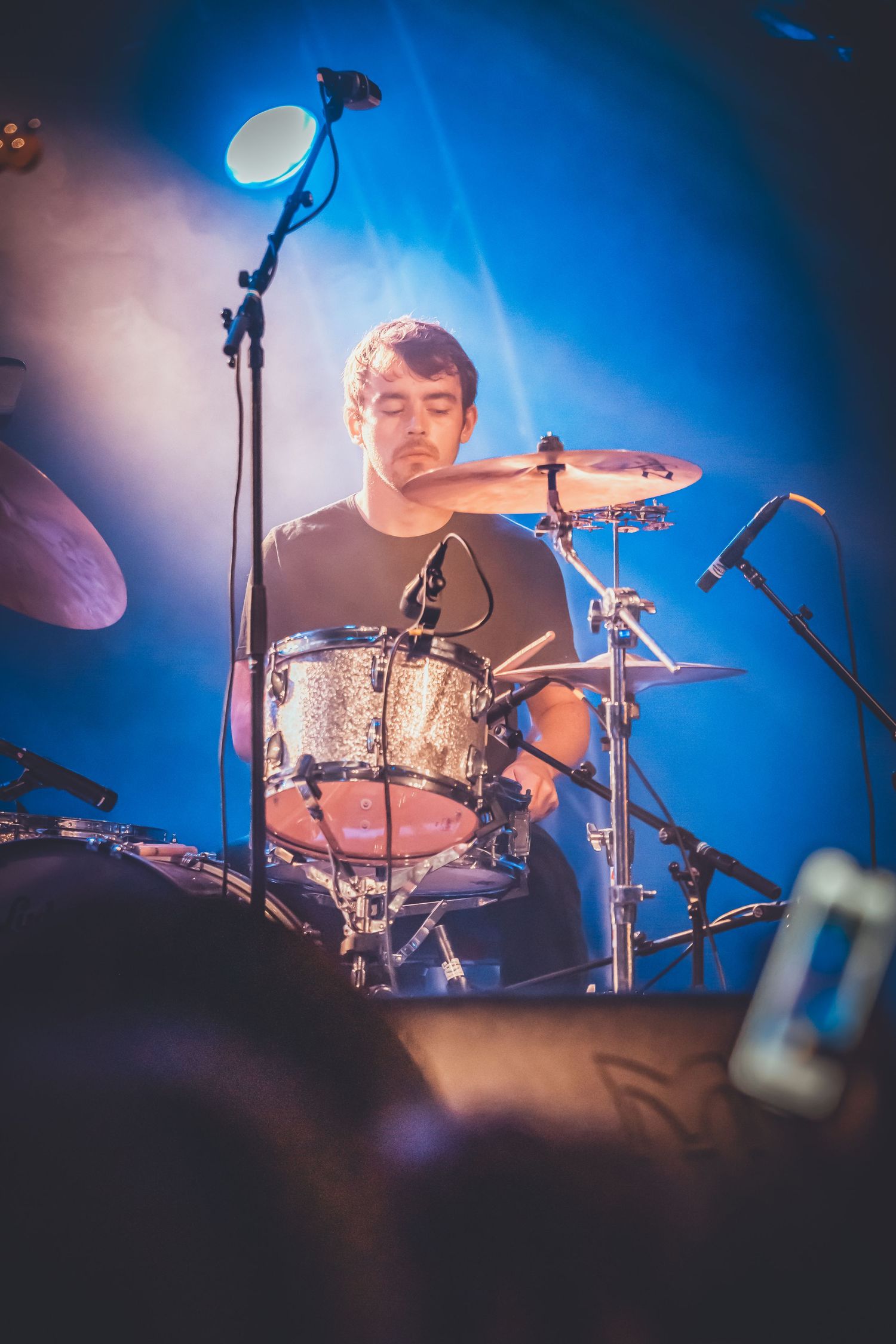 Drummer performs energetically on stage bathed in dramatic blue lighting during a live concert performance.