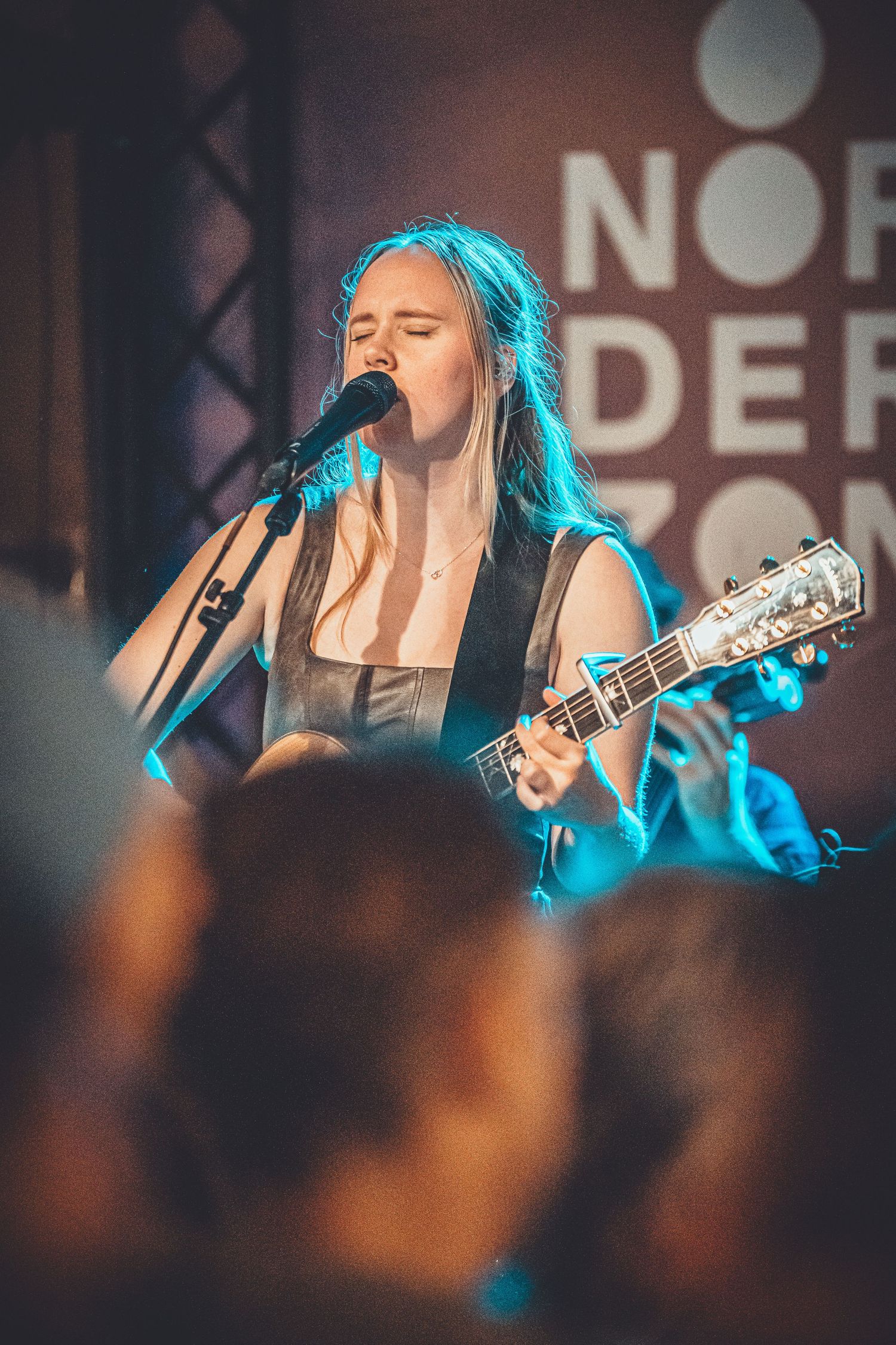 A musician performs on stage with an acoustic guitar under blue lighting during a concert.