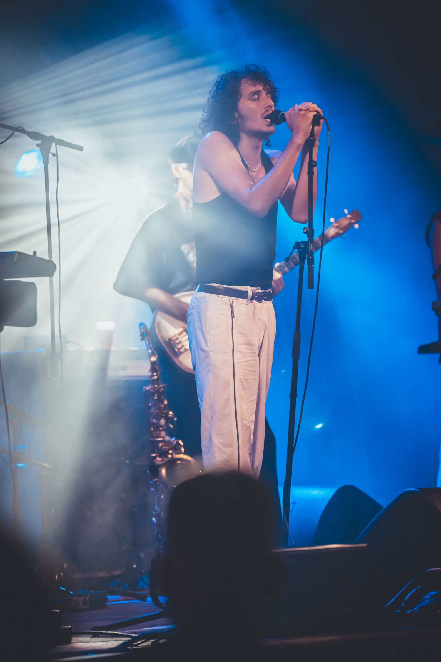 A concert performer in white pants sings passionately on stage with dramatic blue lighting and fog effects in the background.