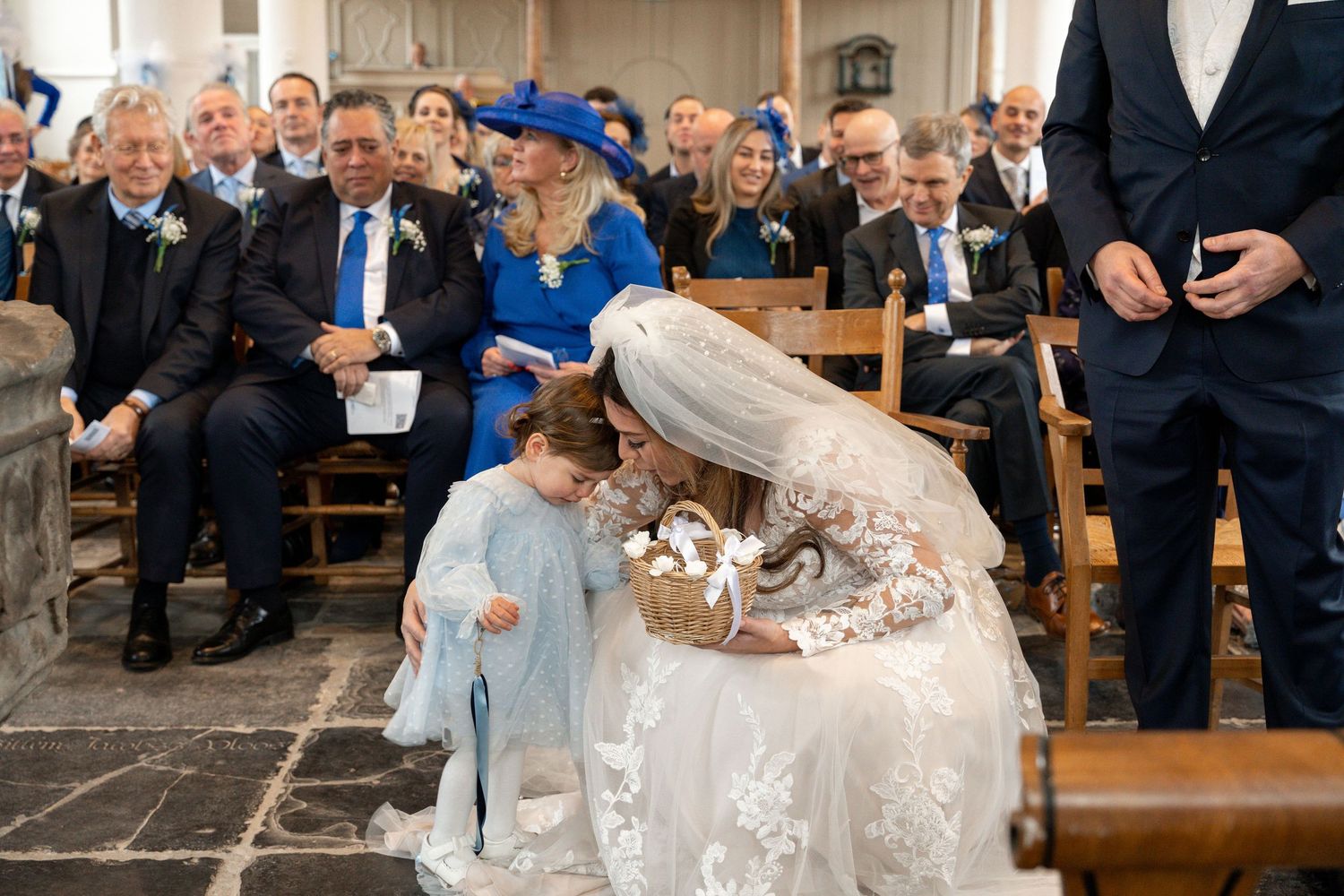 A sweet moment during a church ceremony as a couple interacts tenderly while guests look on from wooden pews.