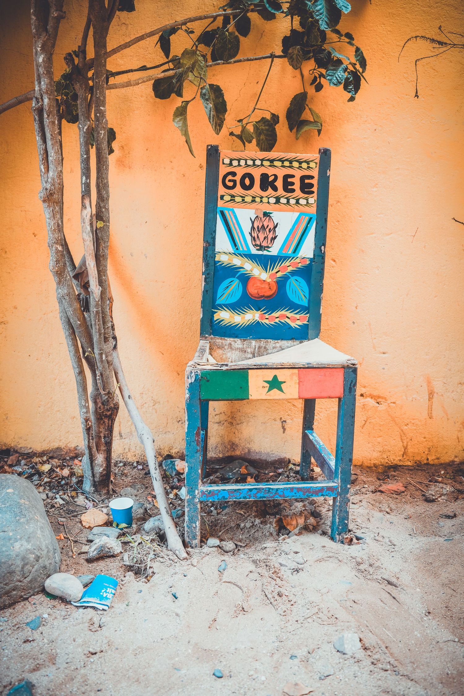 Colorful painted wooden chair with Goree text and Senegal flag against orange wall.