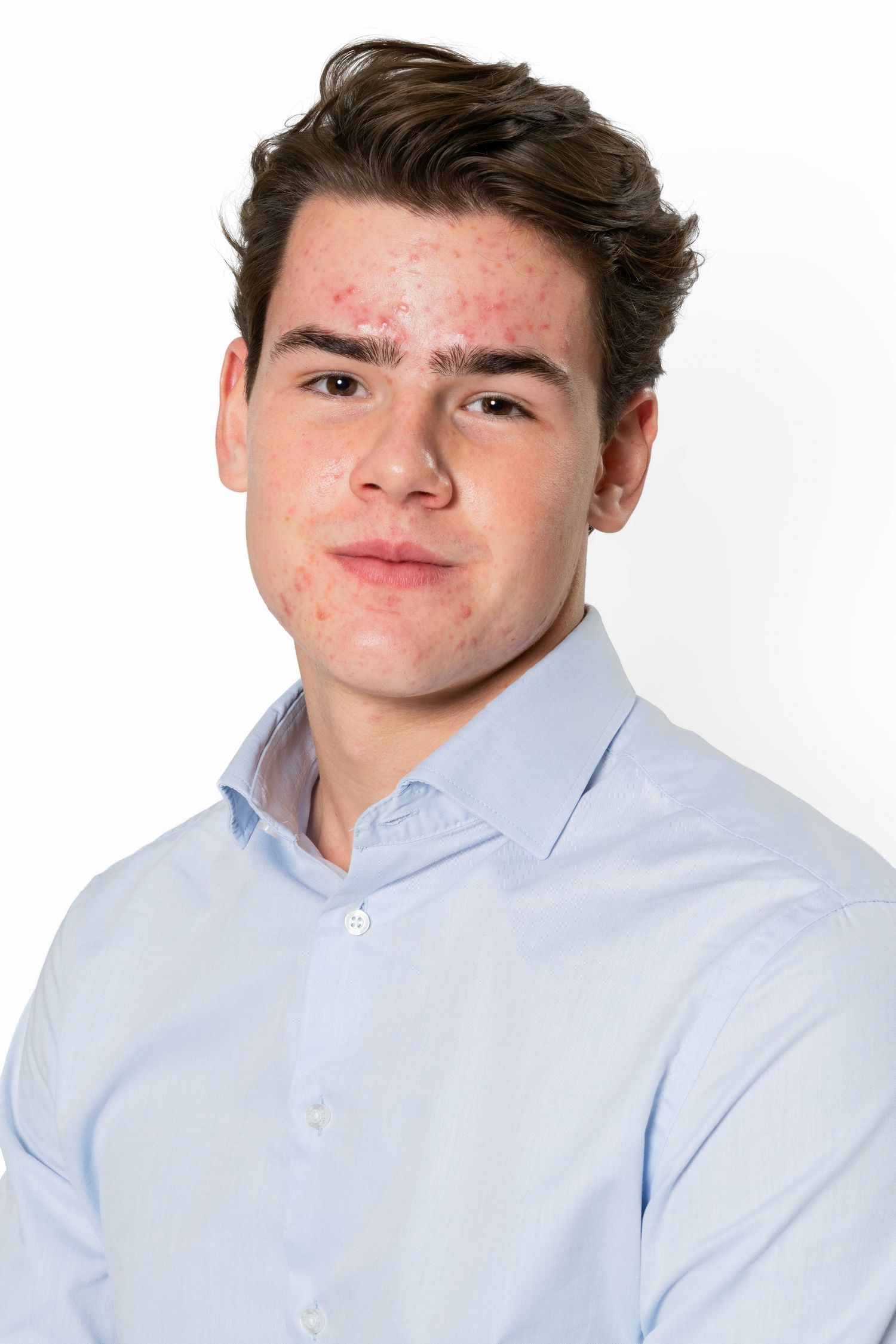Young man with short dark brown hair wearing a light blue collared button-up shirt, posed against a plain white background.
