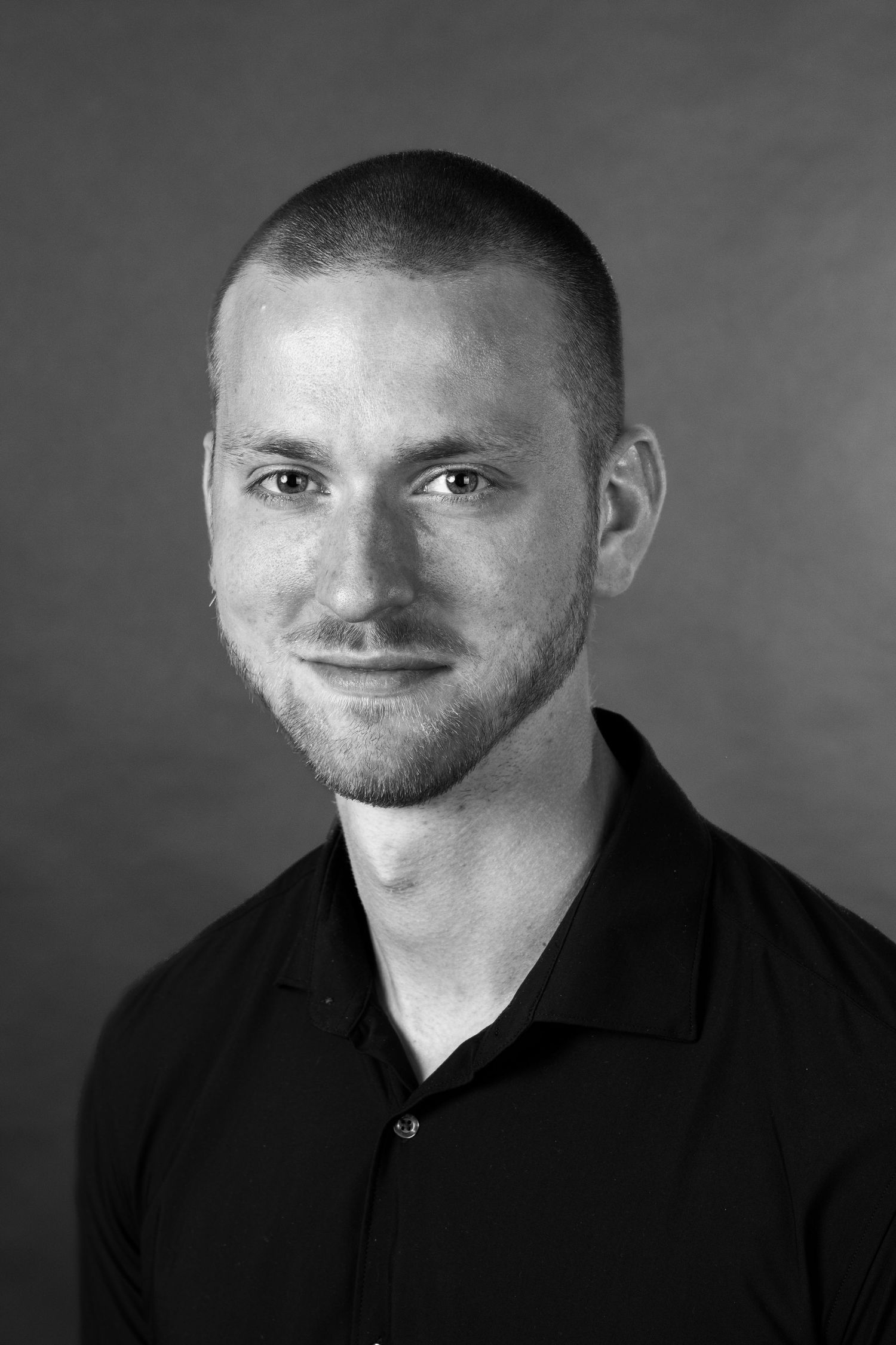 Black and white portrait of a young man with short hair and beard wearing a dark polo shirt.