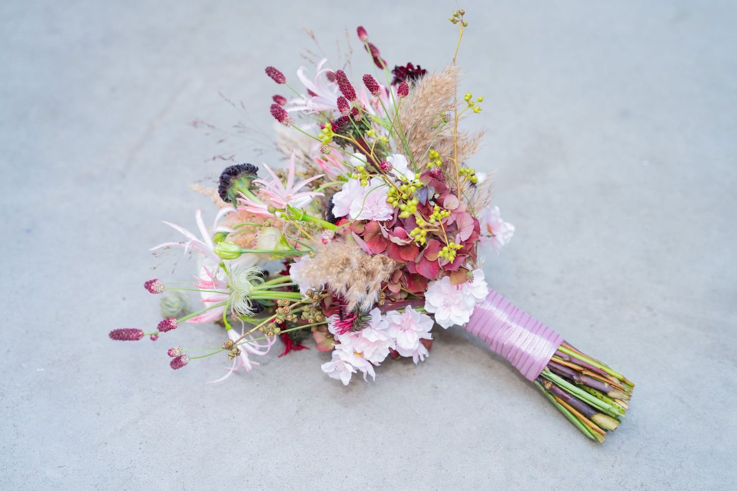 A delicate pink cherry blossom bouquet with white flowers tied with twine is shown from multiple angles on a gray surface.