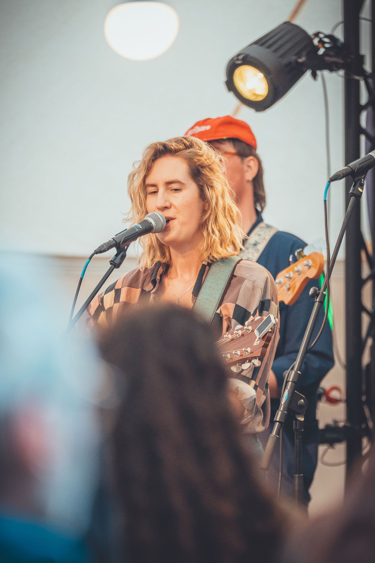 Musician performs on stage with a guitar and microphone under bright spotlights during an outdoor concert performance.