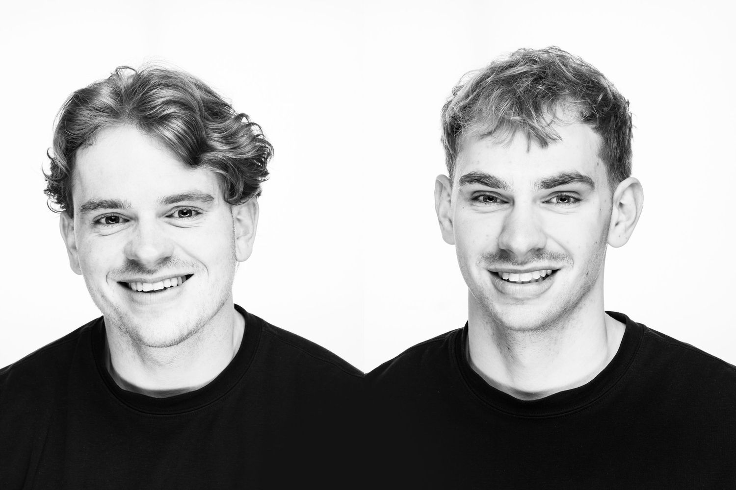 Black and white portrait of two people wearing black shirts smiling against a white background.
