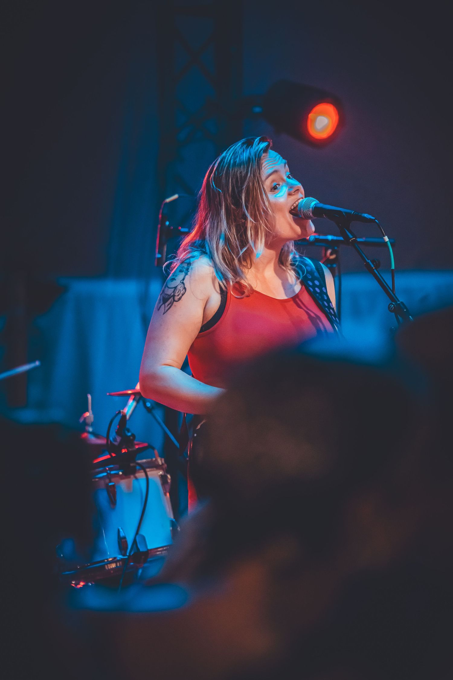 A performer sings passionately on stage bathed in moody red and blue concert lighting during a live music performance.