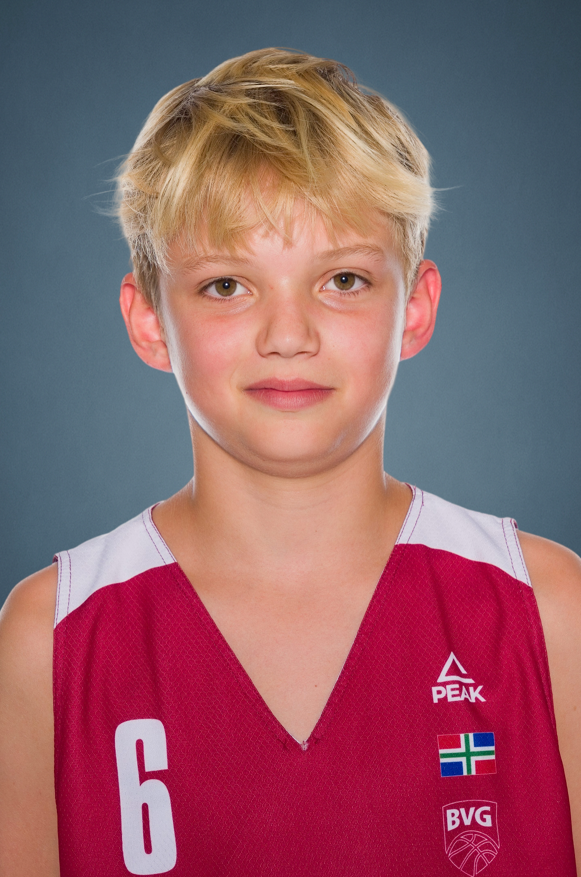Young basketball player with blond hair wearing a red number 6 Peak jersey with BVG logo and a green, white and blue flag patch.
